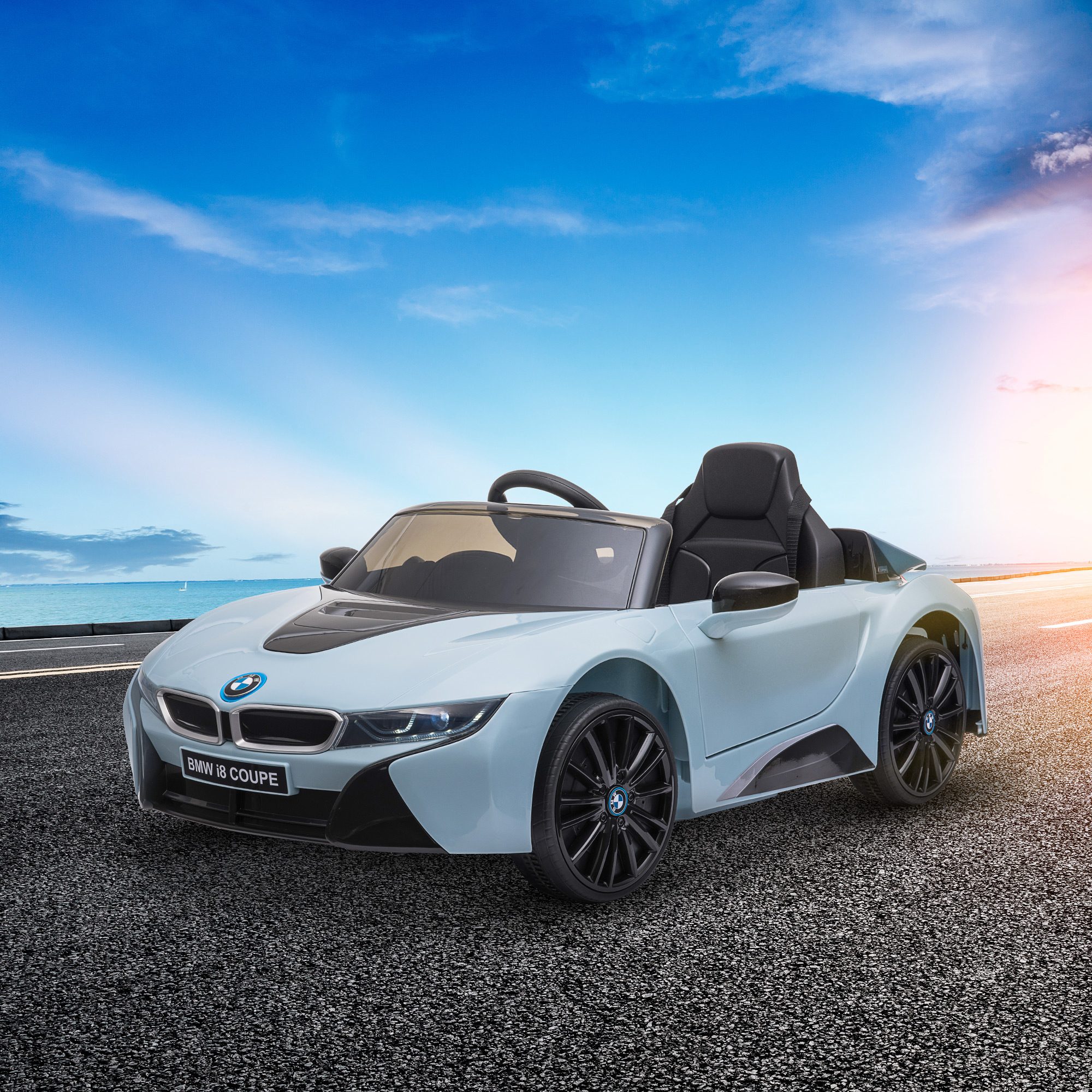 Un'auto giocattolo BMW i8 Coupe azzurra su una strada con cielo soleggiato e oceano sullo sfondo.