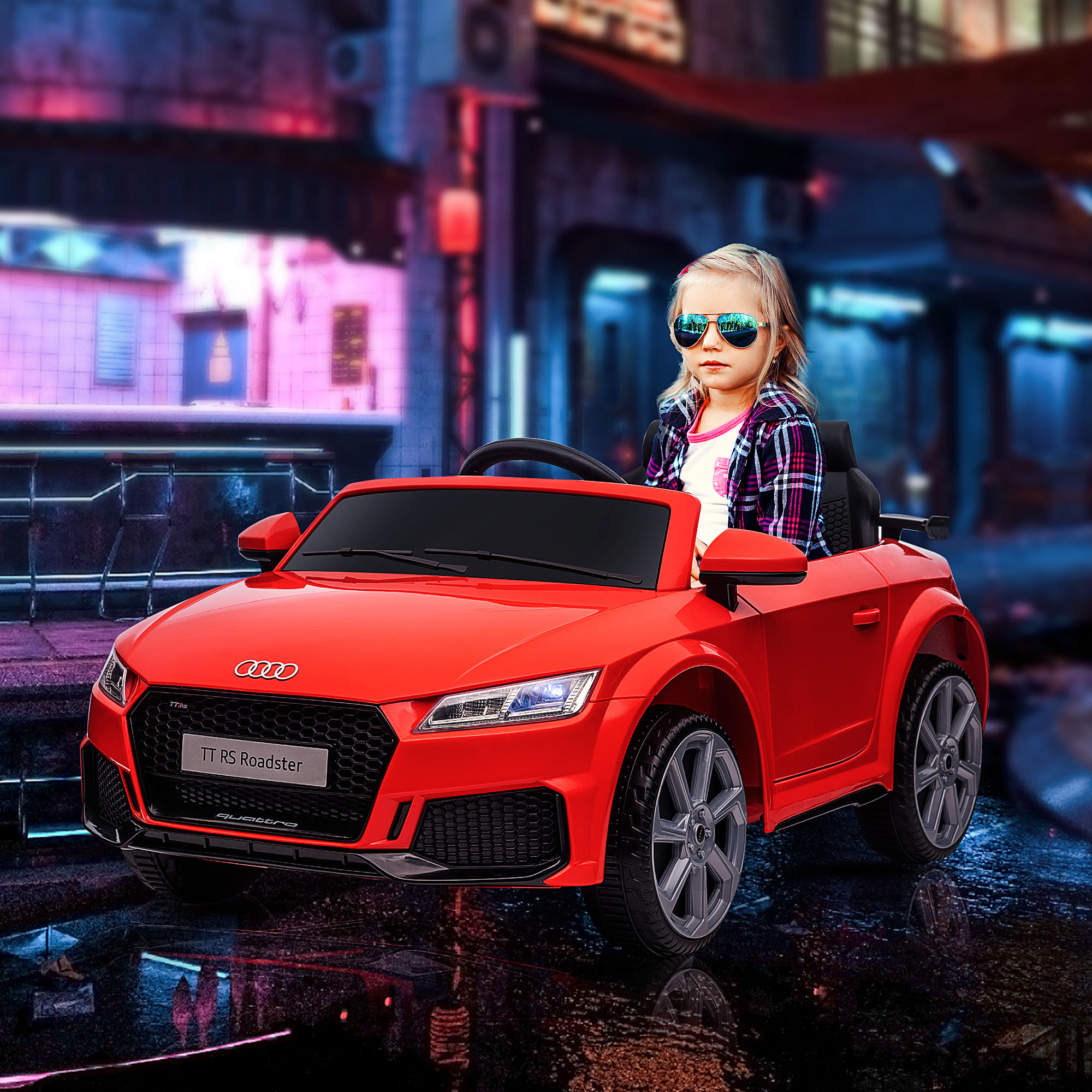 Un bambino con occhiali da sole guida un'auto giocattolo rossa Audi TT RS Roadster su una strada bagnata.