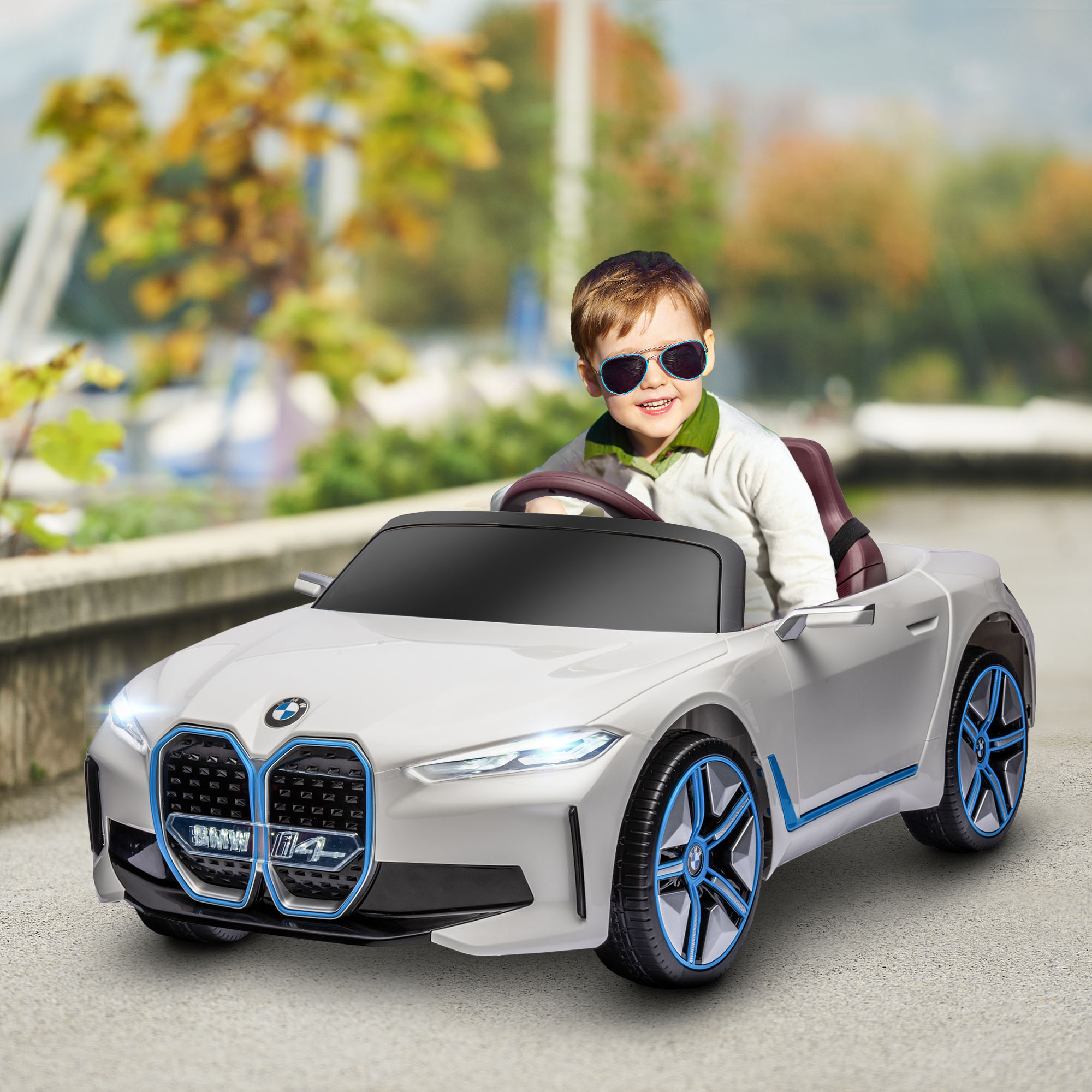 Un bambino con occhiali da sole è seduto in un'auto giocattolo BMW bianca. Dettagli blu e neri sono visibili.