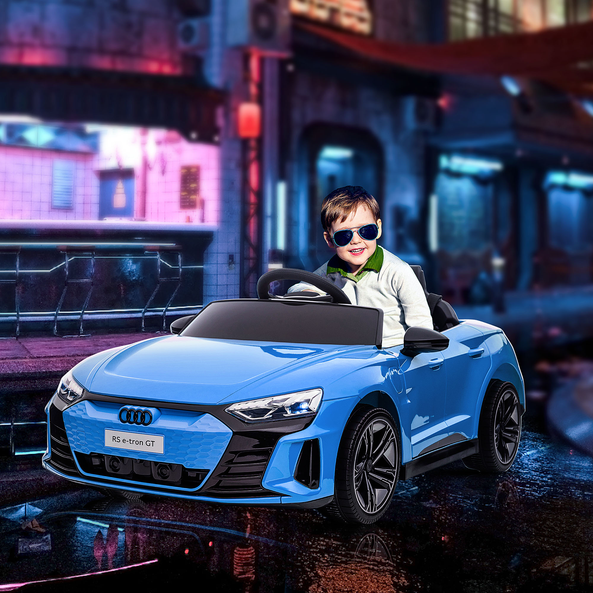 Un ragazzo con gli occhiali da sole è seduto in un'auto giocattolo Audi blu con uno sfondo di strada cittadina notturna.