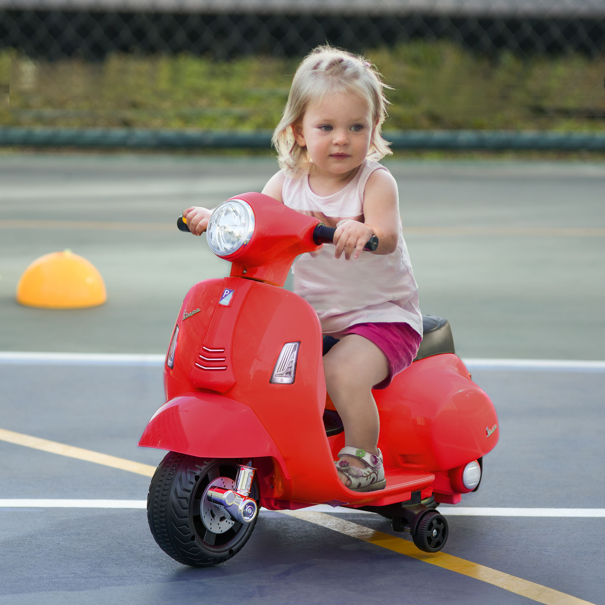 Una bambina su uno scooter Vespa giocattolo rosso su una superficie con linee gialle.
