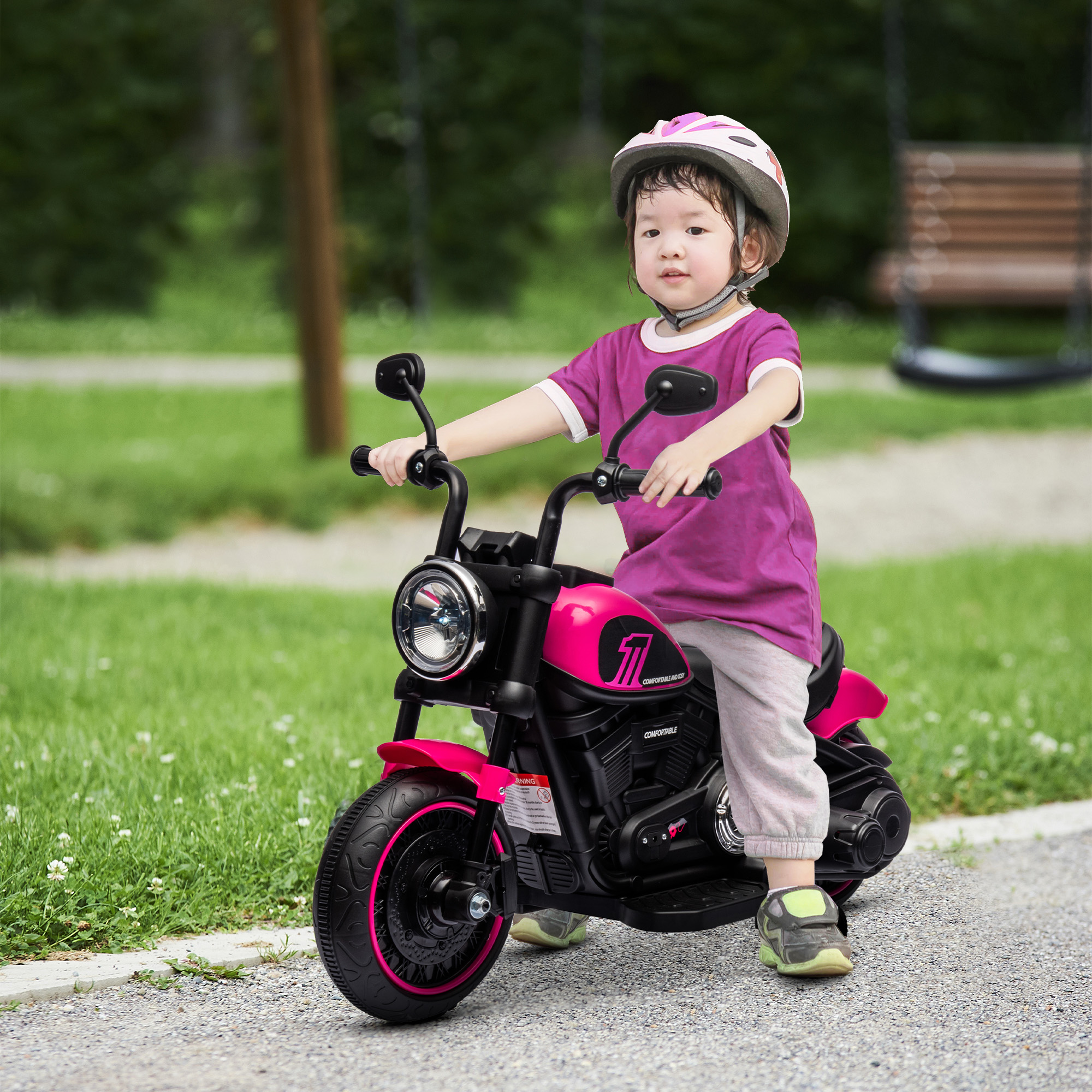 Un niño en una motocicleta rosa. Hierba verde y árboles al fondo.
