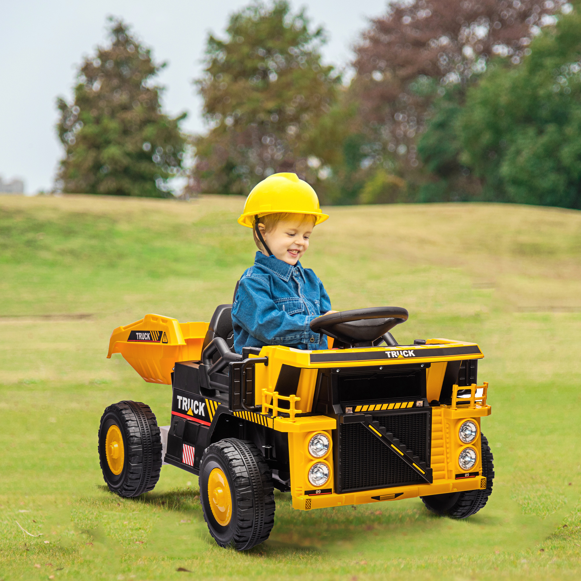 Un bambino in un camion giocattolo giallo e nero. Erba verde e alberi sullo sfondo.