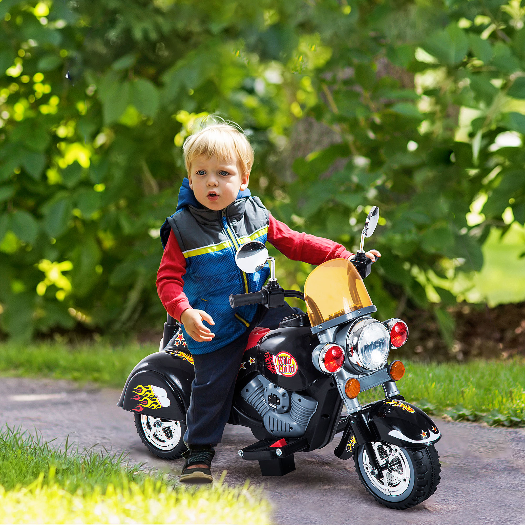 Ragazzino su una moto giocattolo nera e rossa. Sta guardando avanti con uno sfondo verde.