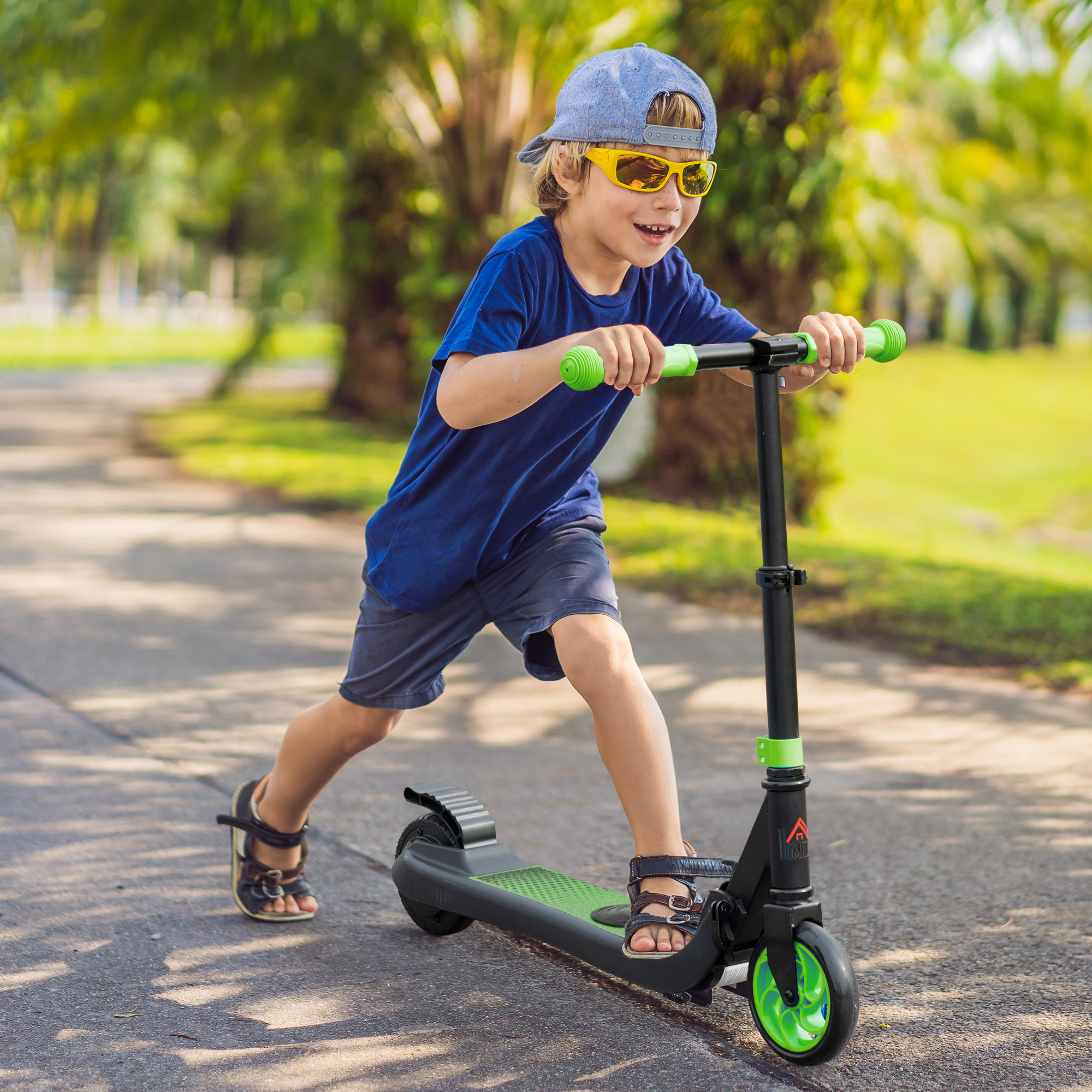 Un ragazzino con occhiali da sole guida un monopattino nero su un sentiero pavimentato nel parco.
