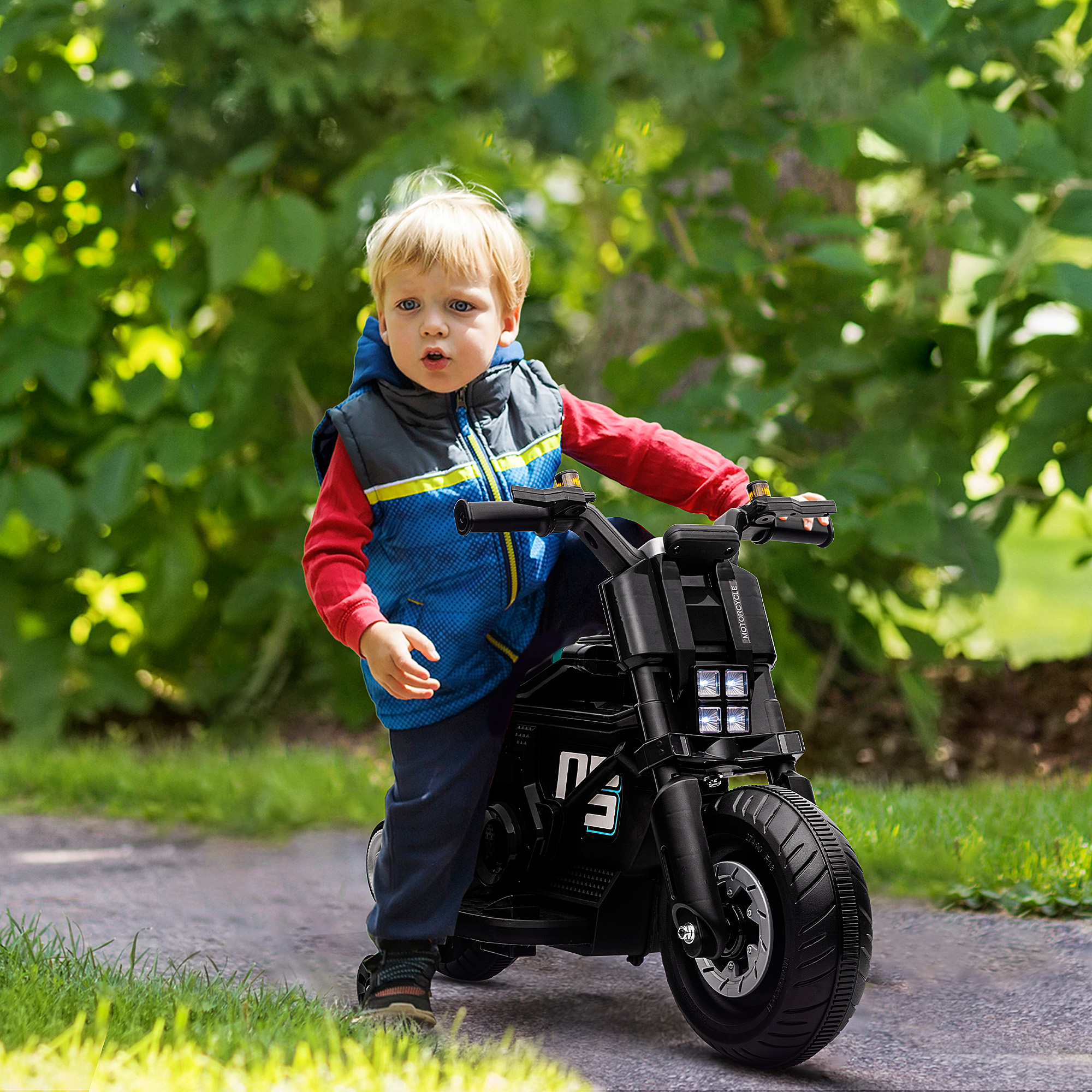 Un bambino su una moto giocattolo nera. Sta guardando verso la telecamera. È visibile erba verde.