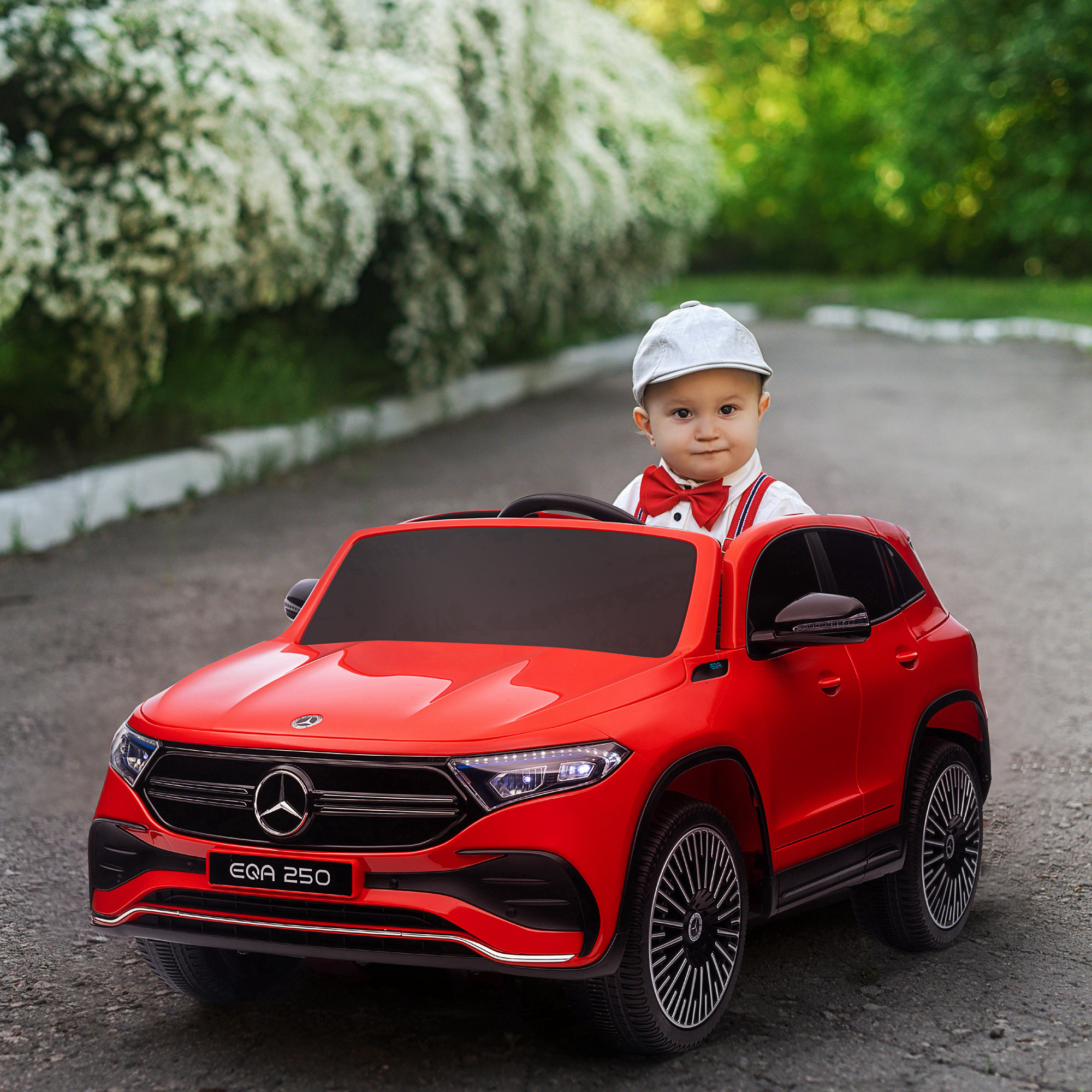 Bambino in auto giocattolo rossa. Auto rossa, camicia bianca, papillon, cappello grigio. Sulla strada in un parco.