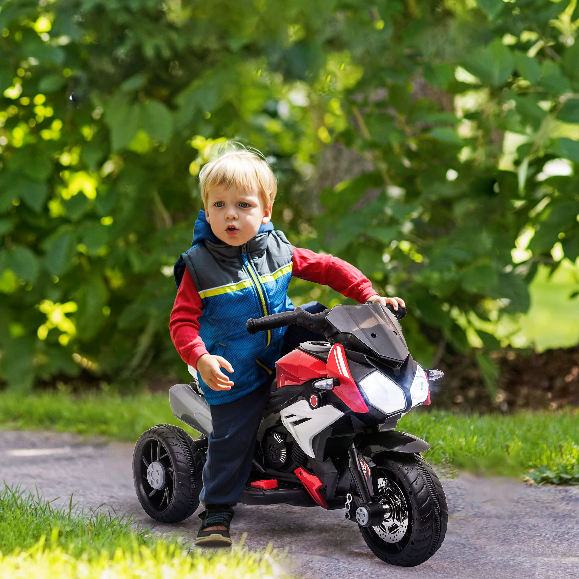 Bambino piccolo su una moto giocattolo rossa e nera. Lo sfondo è un fogliame verde.