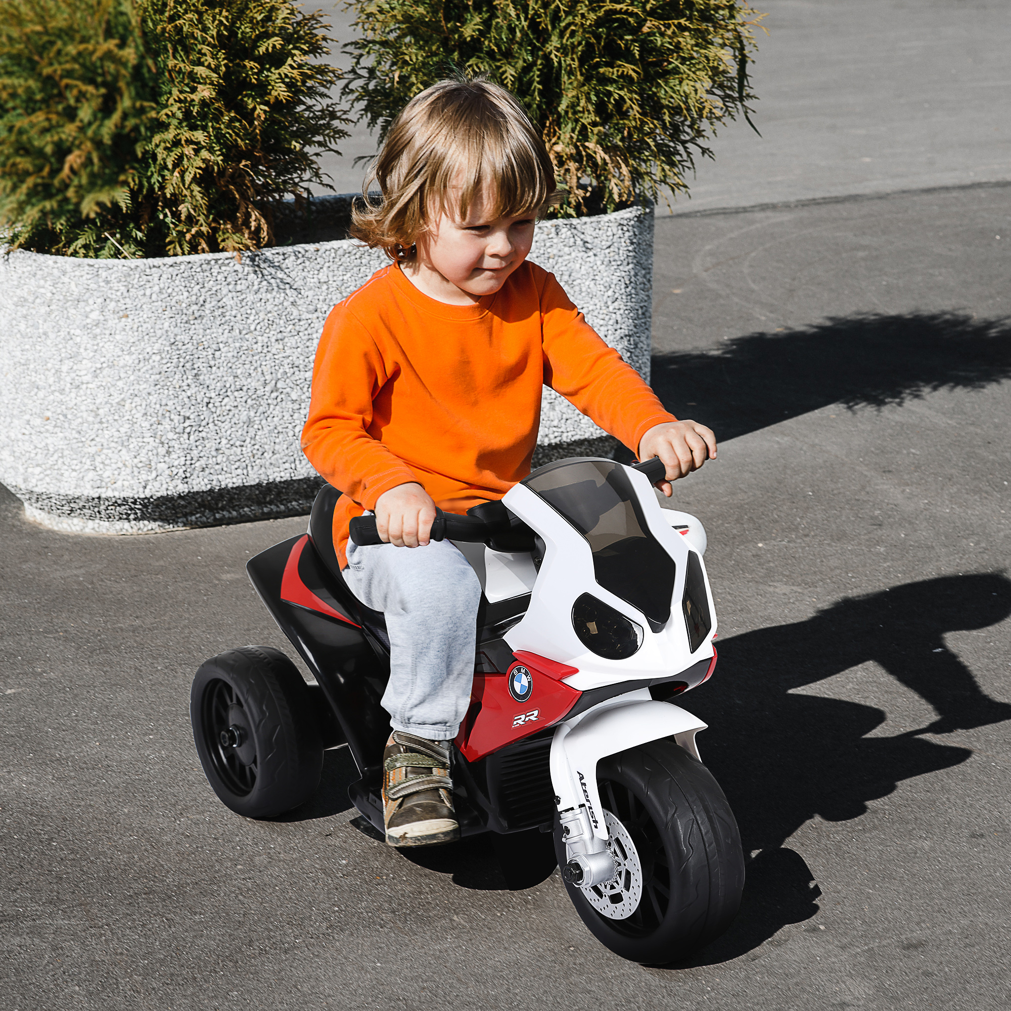 Un bambino piccolo guida una moto giocattolo BMW bianca e rossa sulla strada.