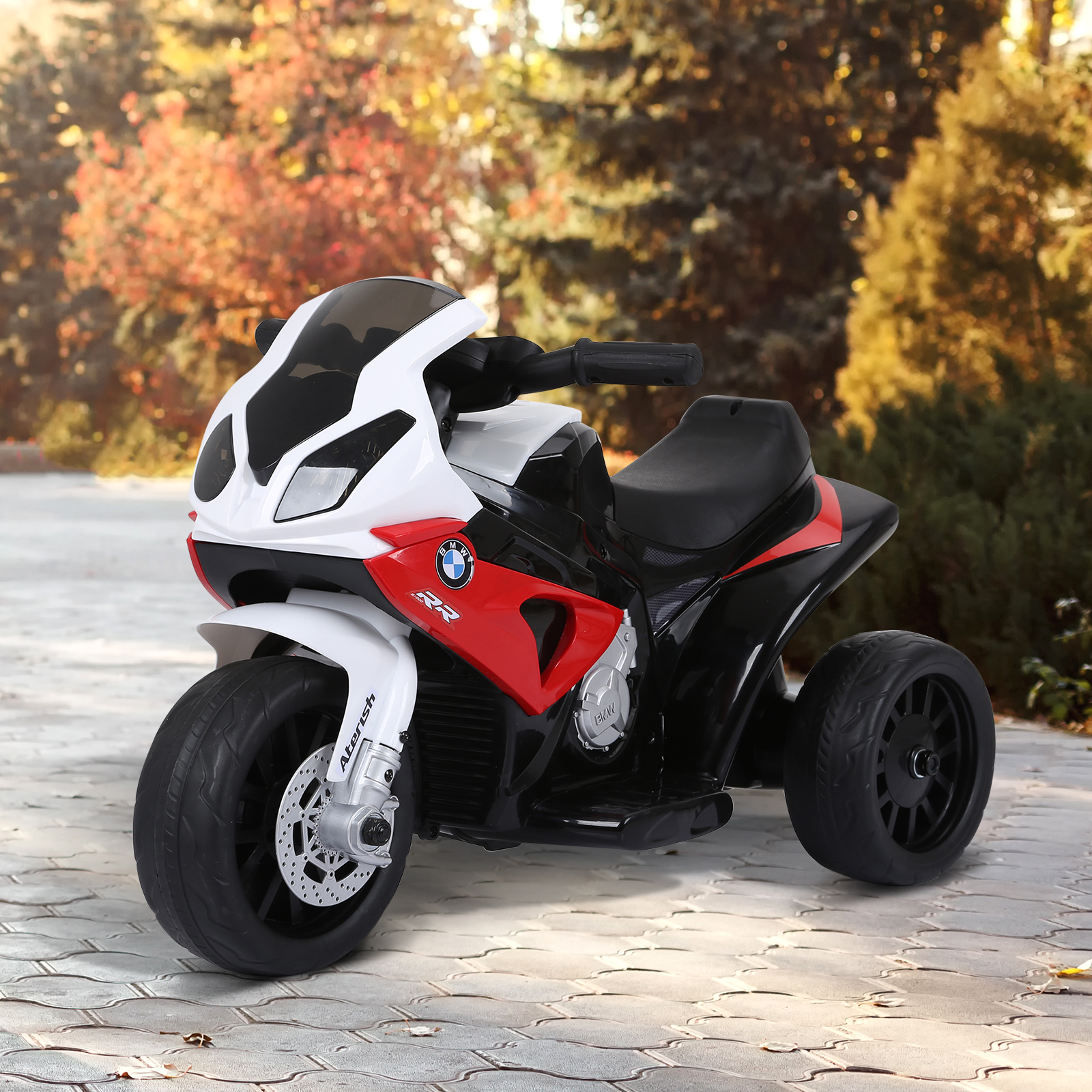 Una moto giocattolo rossa, bianca e nera è parcheggiata su una superficie pavimentata, con alberi sullo sfondo.