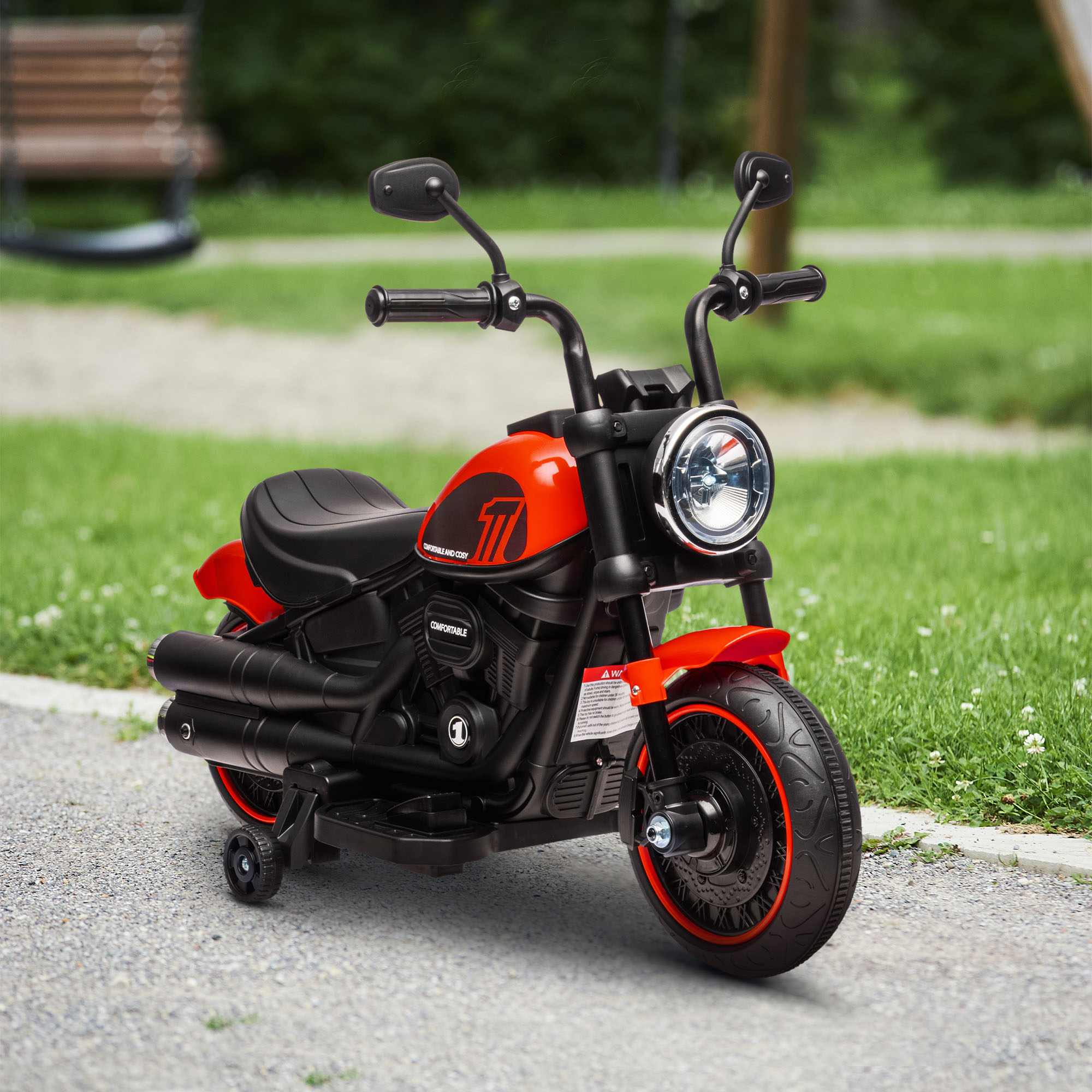 Moto giocattolo rossa con dettagli neri, faro rotondo e rotelle. Sentiero di ghiaia, erba verde.