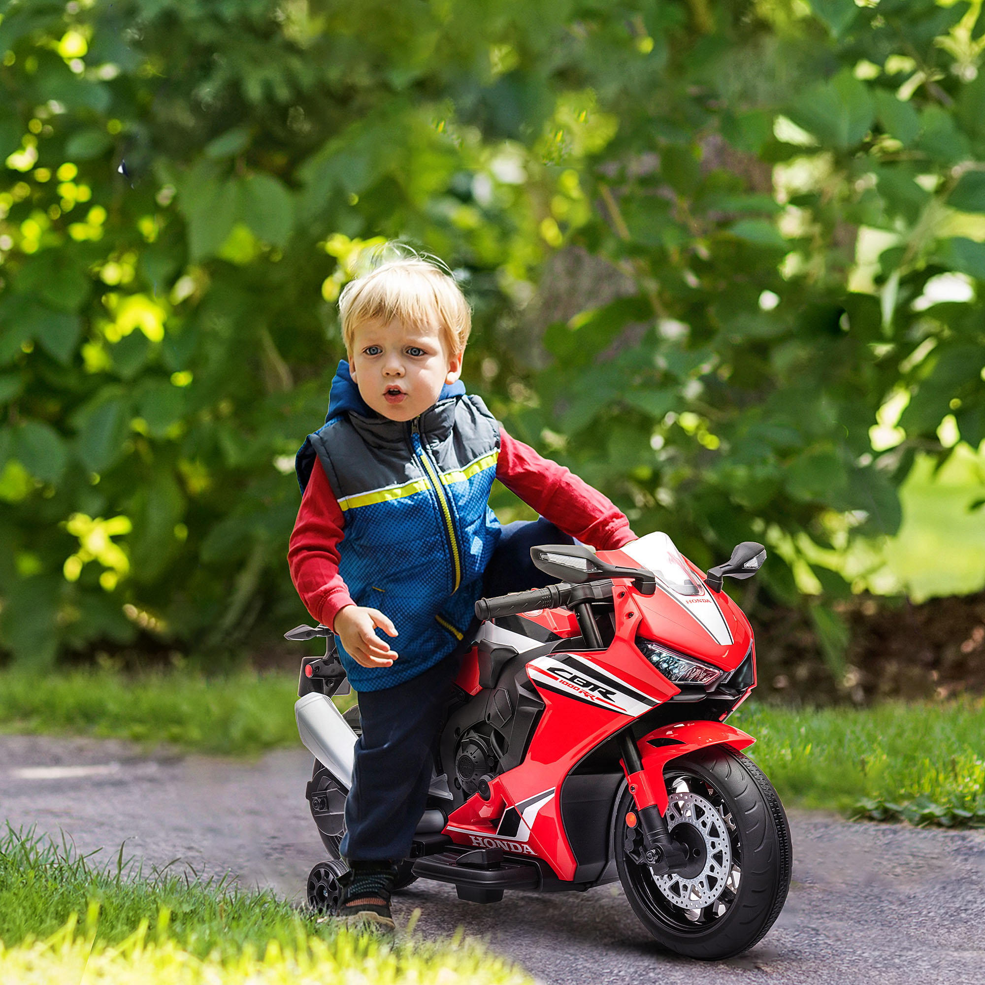 Un bambino su una moto giocattolo rossa. Alberi verdi sullo sfondo.