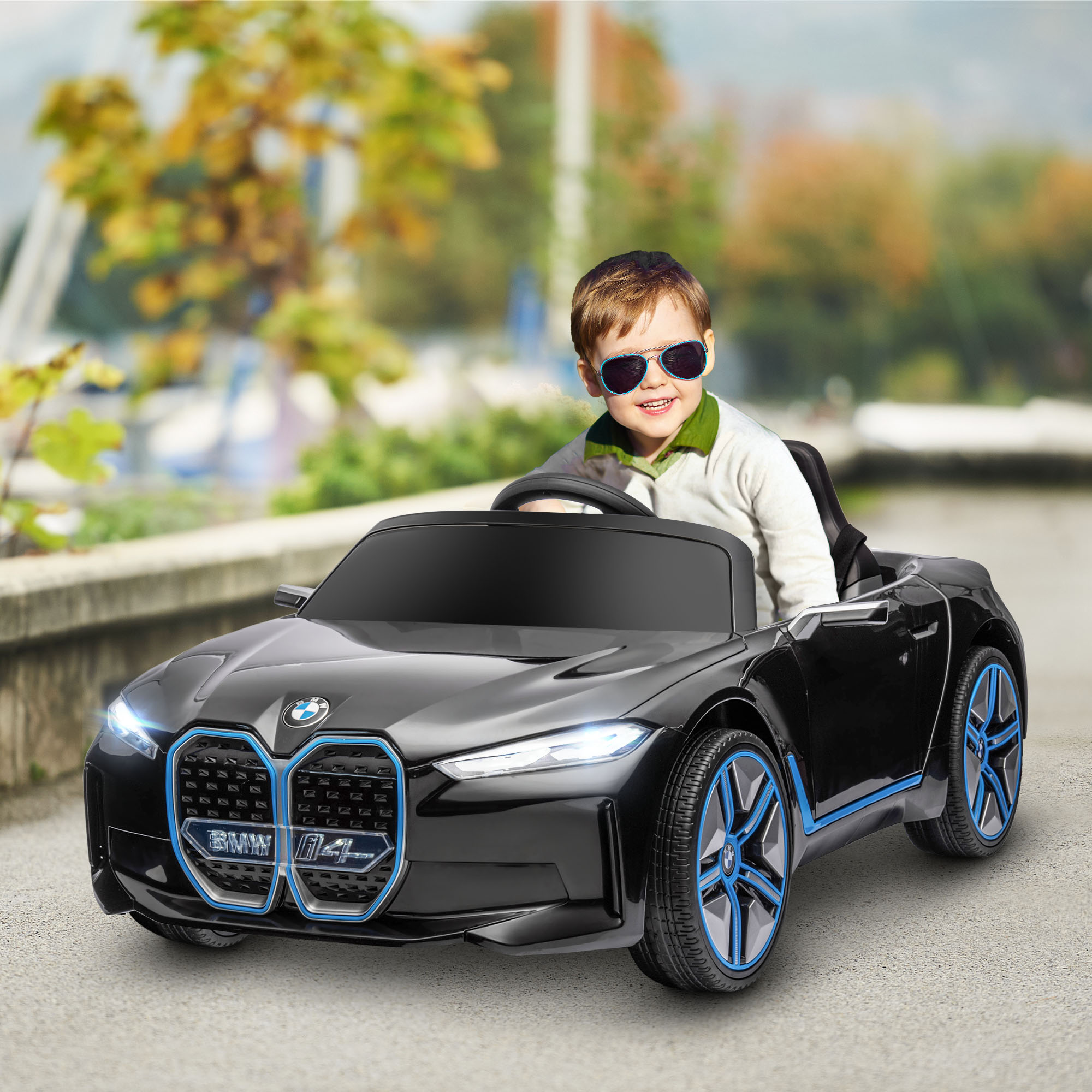 Un bambino in un'auto giocattolo nera. Sfondo sfocato di alberi e strada.