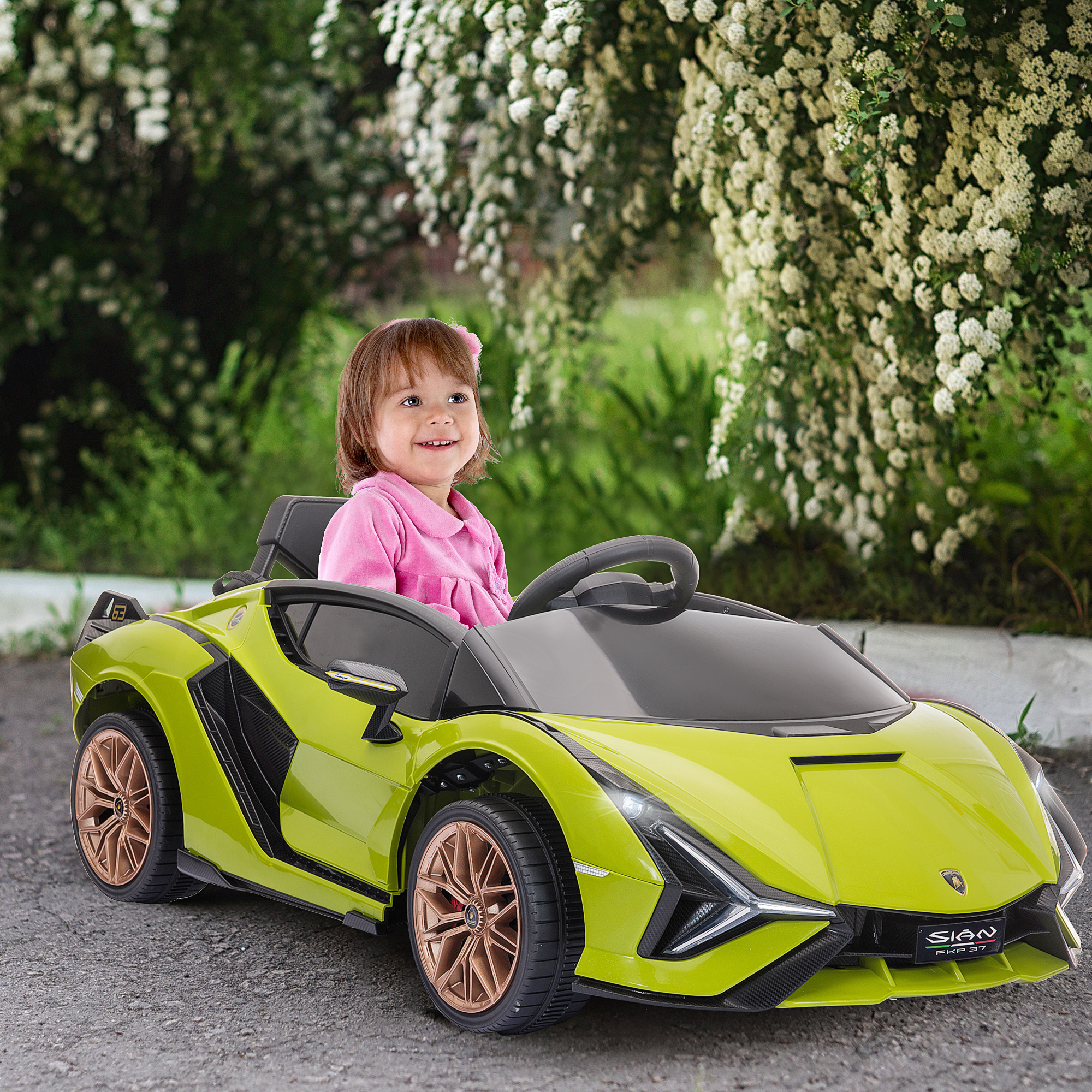 Un bambino sorride seduto in un'auto giocattolo gialla. Ci sono fiori sullo sfondo.