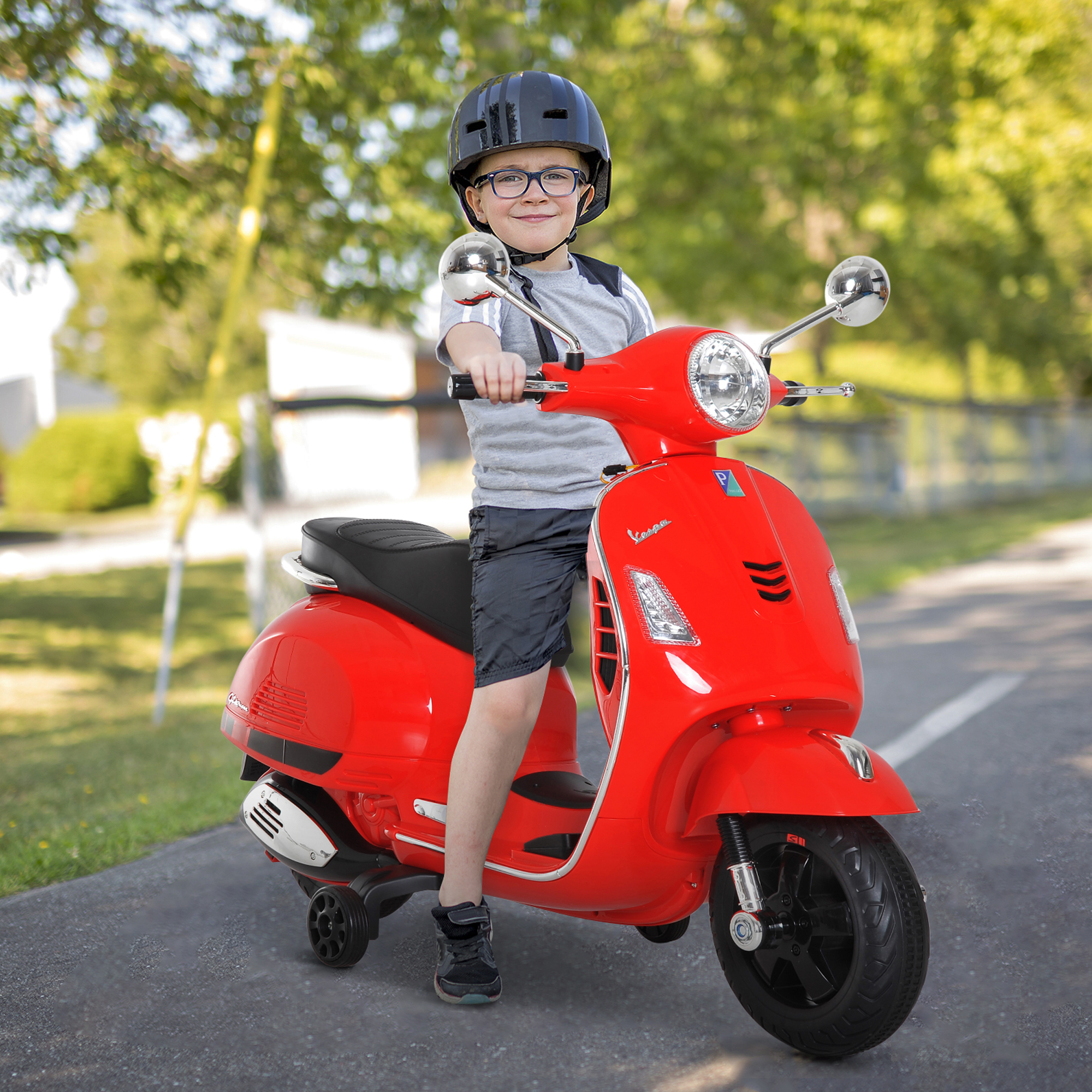 Ragazzo su una Vespa giocattolo rossa su una strada. Sfondo: alberi e cielo.