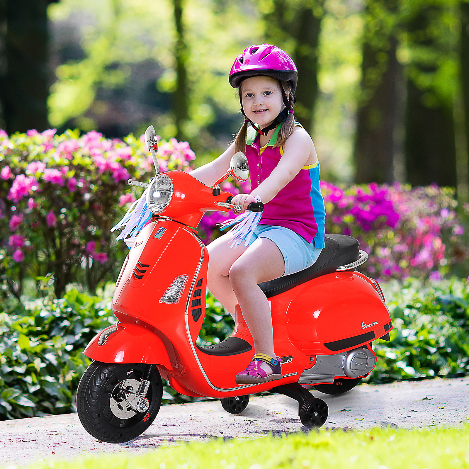 Una bambina con un casco rosa guida uno scooter Vespa rosso su un sentiero pavimentato in un parco.