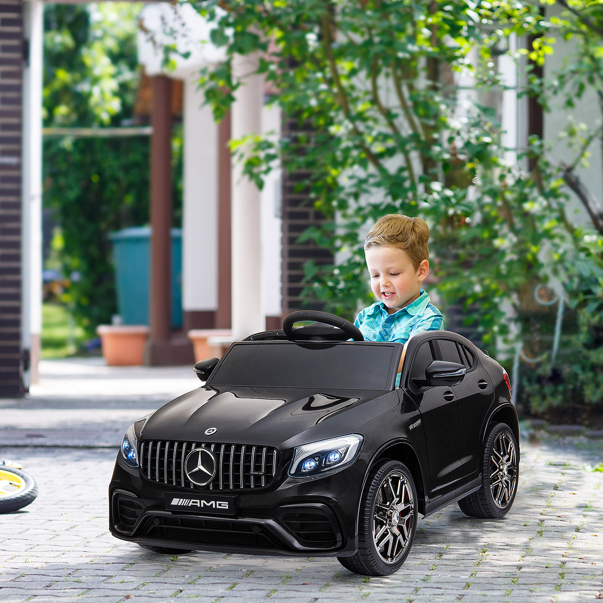 Un bambino sorride mentre guida un'auto giocattolo nera. Lo sfondo è un patio in mattoni.