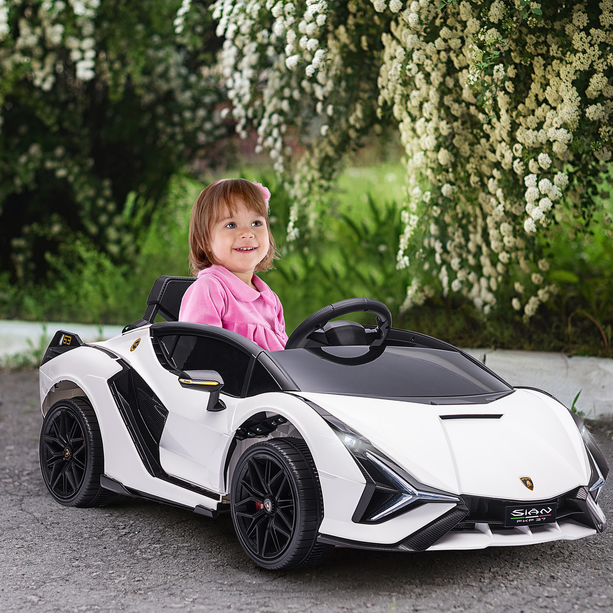Una bambina guida un'auto giocattolo bianca, sorridendo, con sfondo naturale.