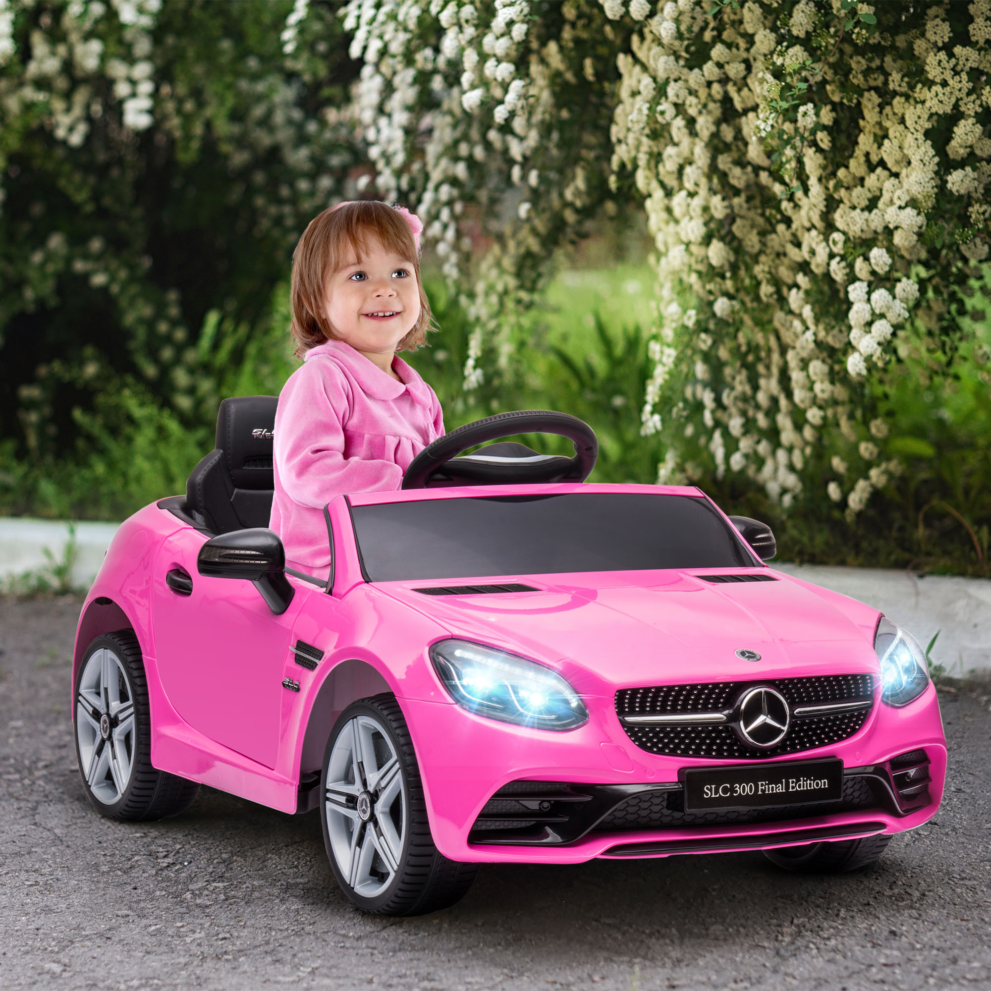Una niña en un atuendo rosa conduce un coche de juguete rosa. Fondo: parque verde con flores blancas.