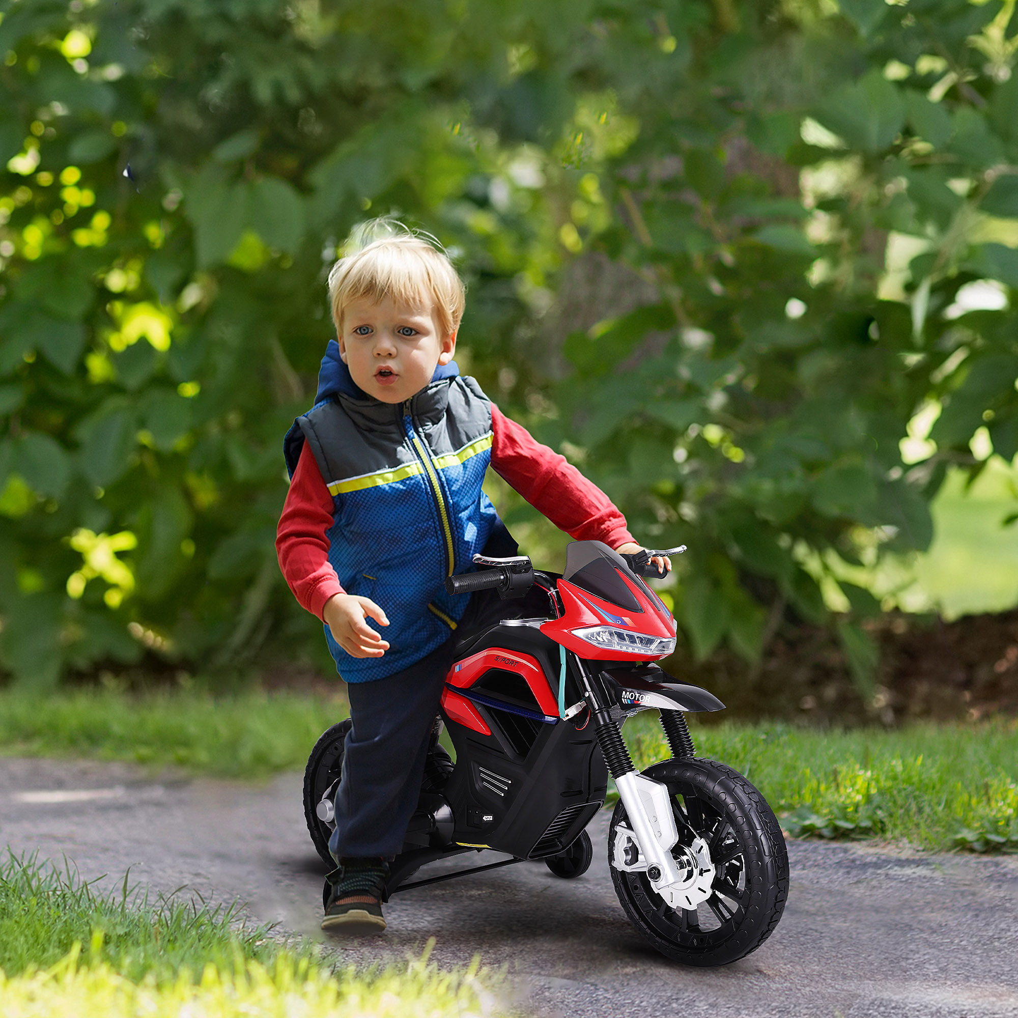 Bambino su moto giocattolo rossa e nera. Sfondo di fogliame verde.