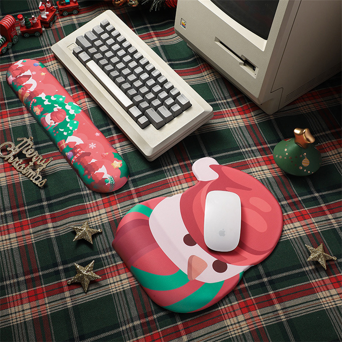 Weihnachts-Schreibtisch-Setup: Tastatur, Maus, Handgelenkstütze, Santa-Matte, Ornamente und Computer auf karierter Oberfläche.