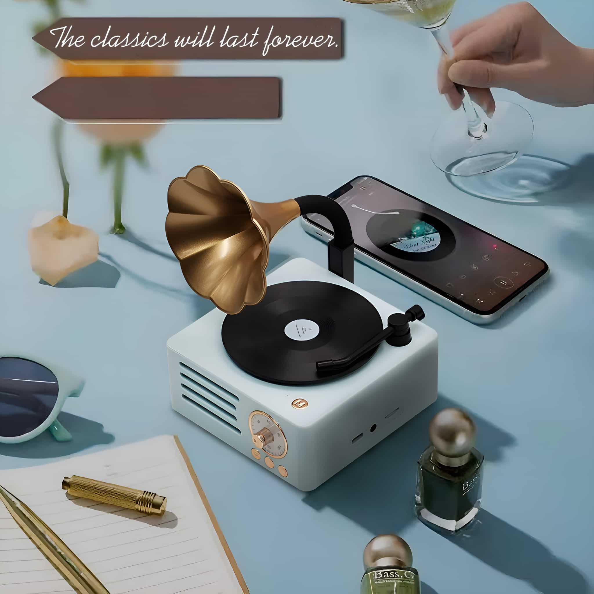 Lautsprecher im Vintage-Grammofon-Stil, abspielendes Handy, Parfümflaschen und Stift auf blauer Oberfläche.