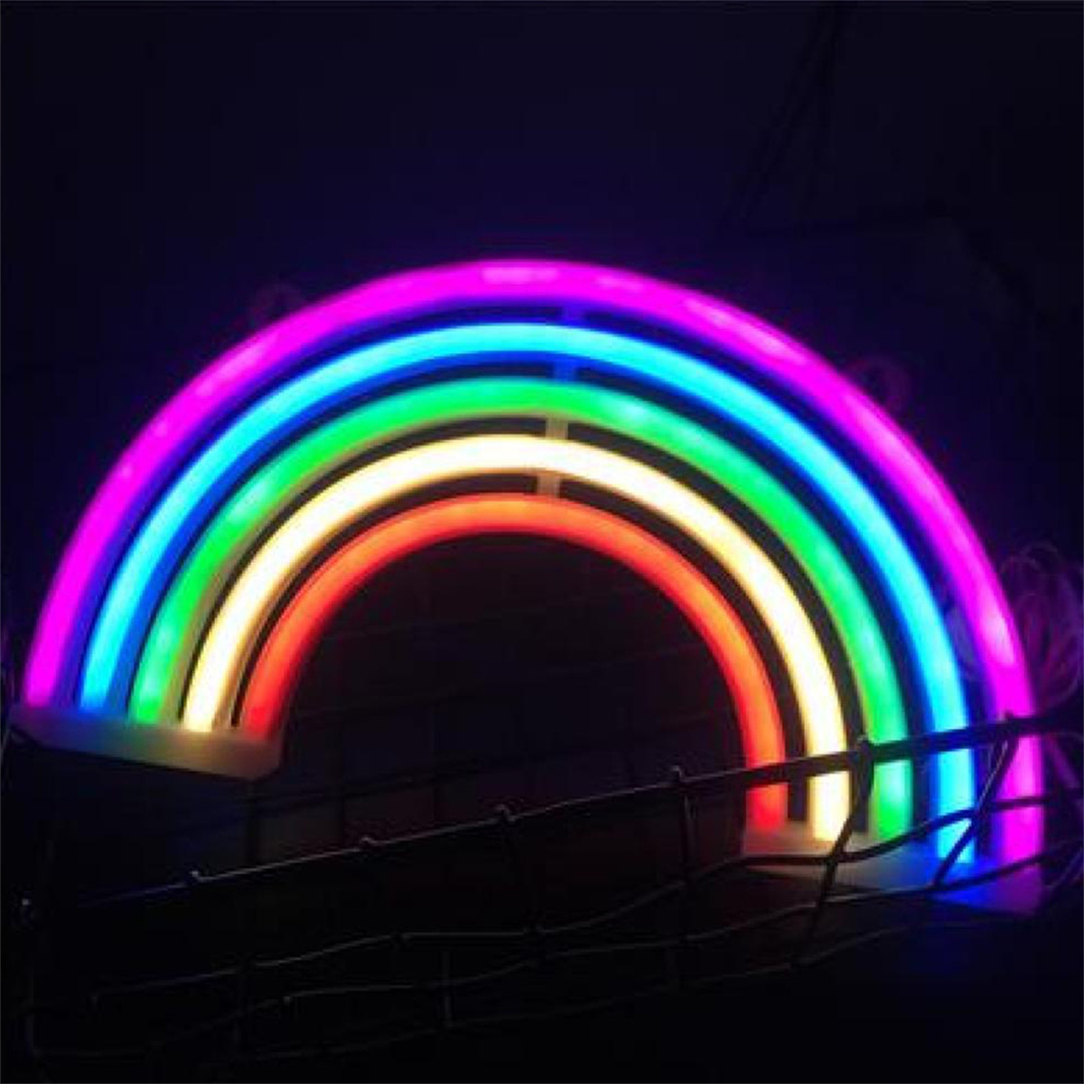 Ein Neon-Regenbogen mit mehreren Farben, der auf dunklem Hintergrund hängt. Es ist ein Dekorationsartikel.