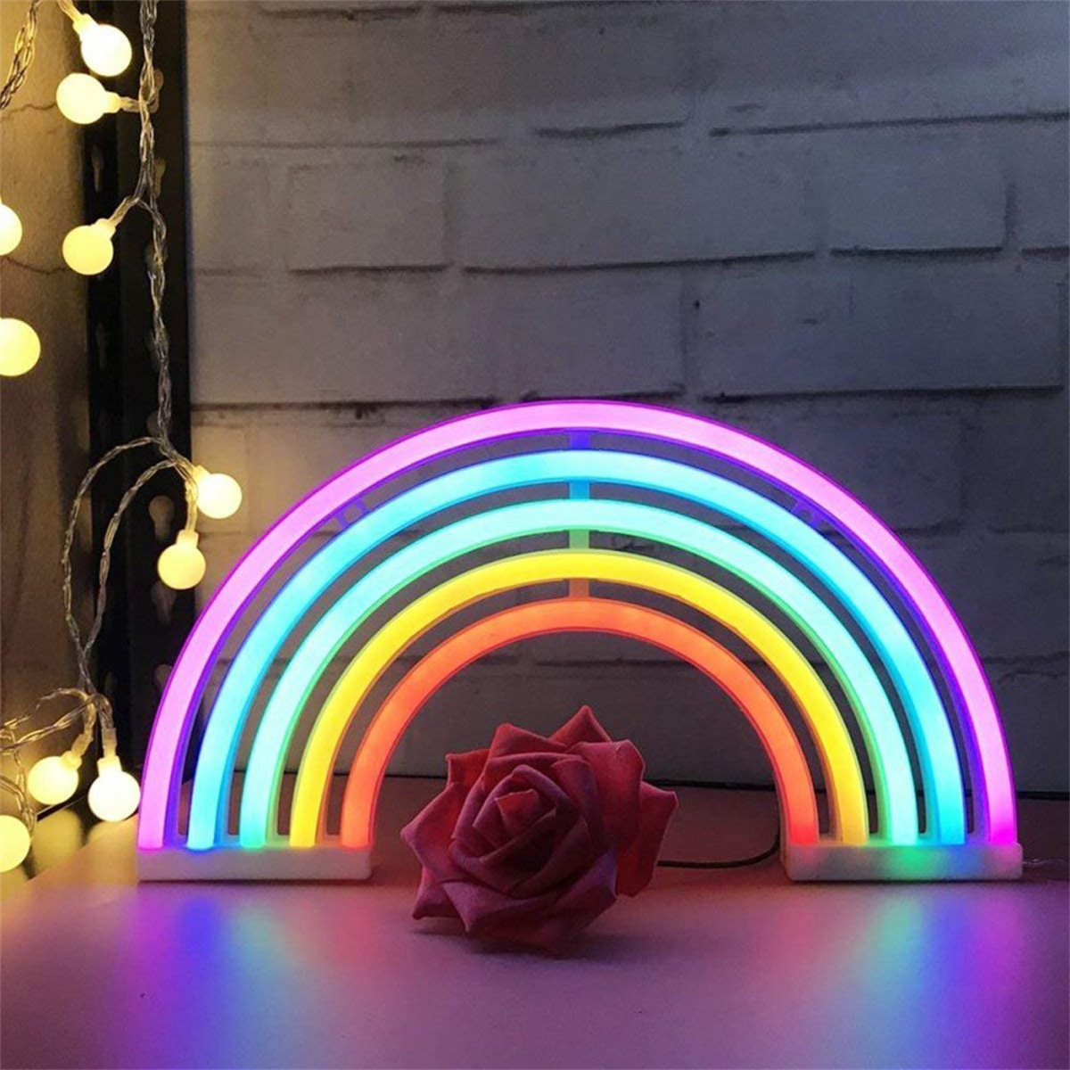 Regenbogen-Neonlicht und eine rote Rose auf dunkler Oberfläche mit Lichterketten.