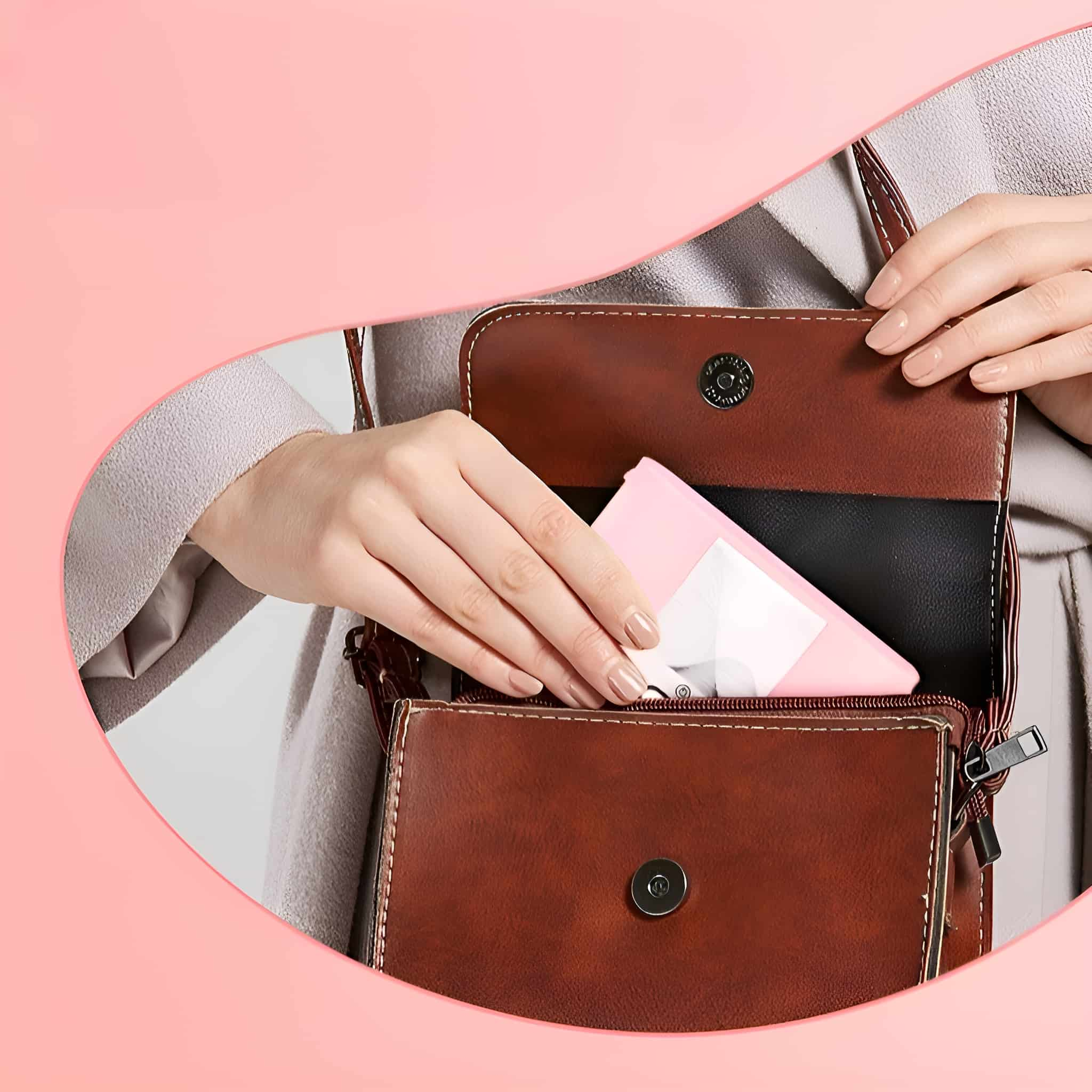 Die Hand einer Person greift in eine braune Handtasche und nimmt ein kleines rosa Päckchen heraus.