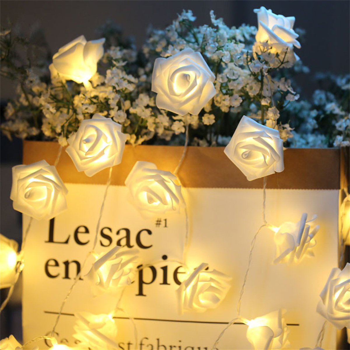 Weiße rosenförmige Lichter an einer Schnur, in einer Papiertüte mit Text und weißen Blumen.