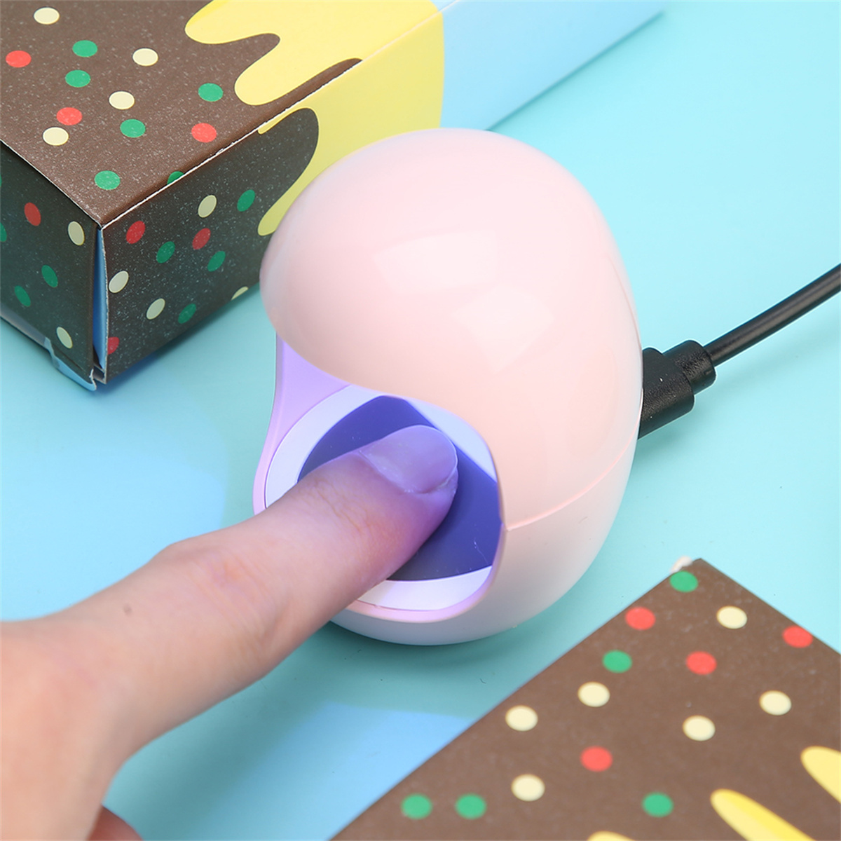 Rosa Nageltrockner mit Finger, auf blauer Oberfläche mit Geschenkboxen.