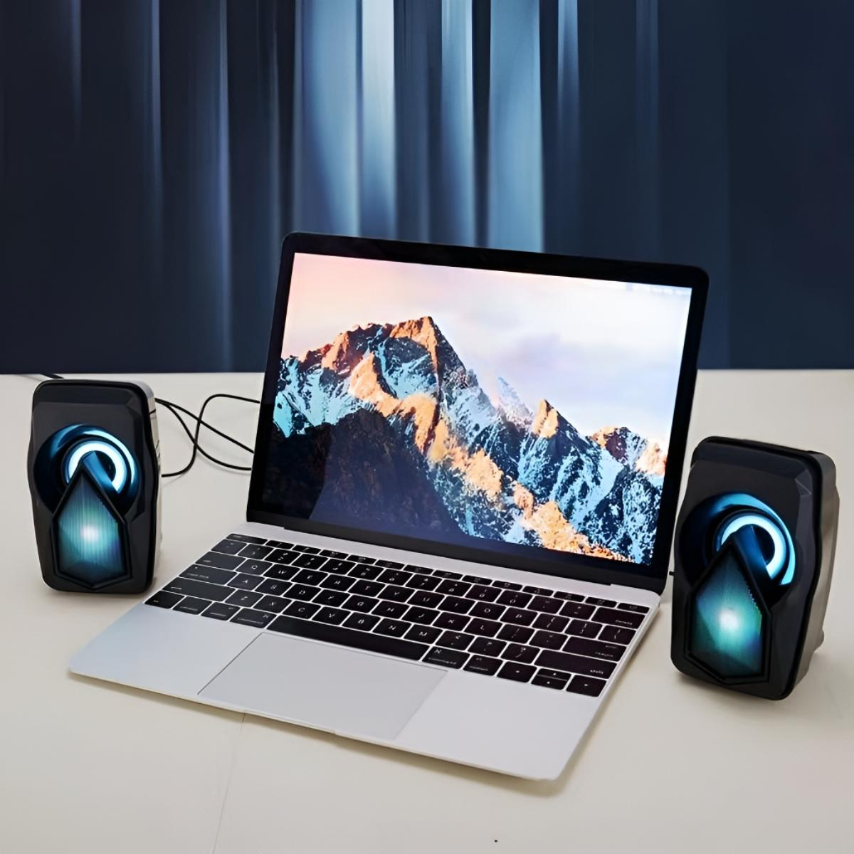 Ein Laptop, flankiert von zwei schwarzen Lautsprechern mit blauem Licht. Ein Bergpanorama ist auf dem Bildschirm.