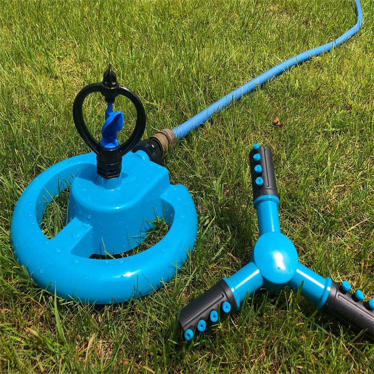 Blauer und schwarzer Rasensprenger mit Wasserschlauch auf grünem Gras. Sonniger Tag.