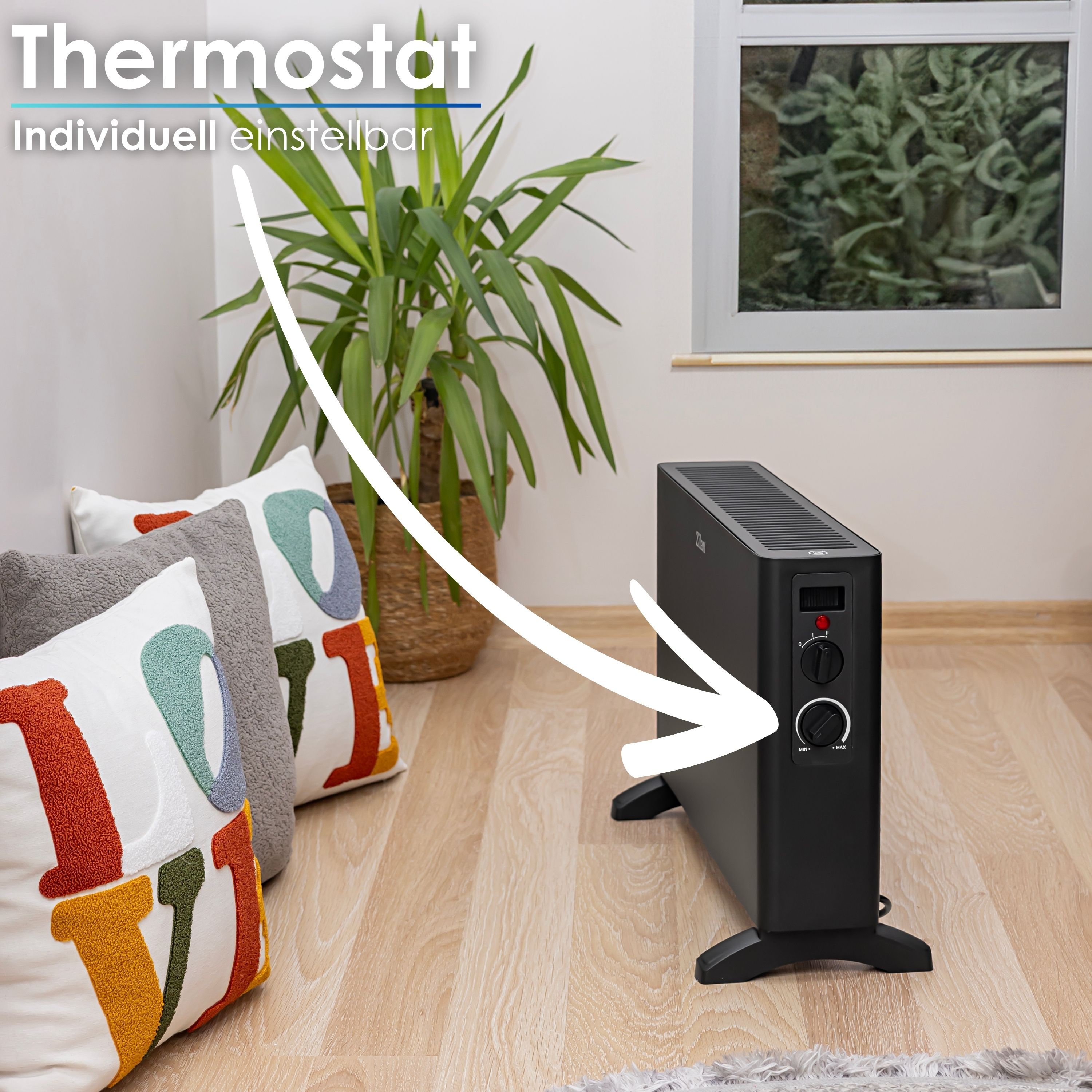 Schwarzer Heizlüfter mit Thermostat, drinnen in der Nähe einer Pflanze und Kissen, mit weißem Pfeil.
