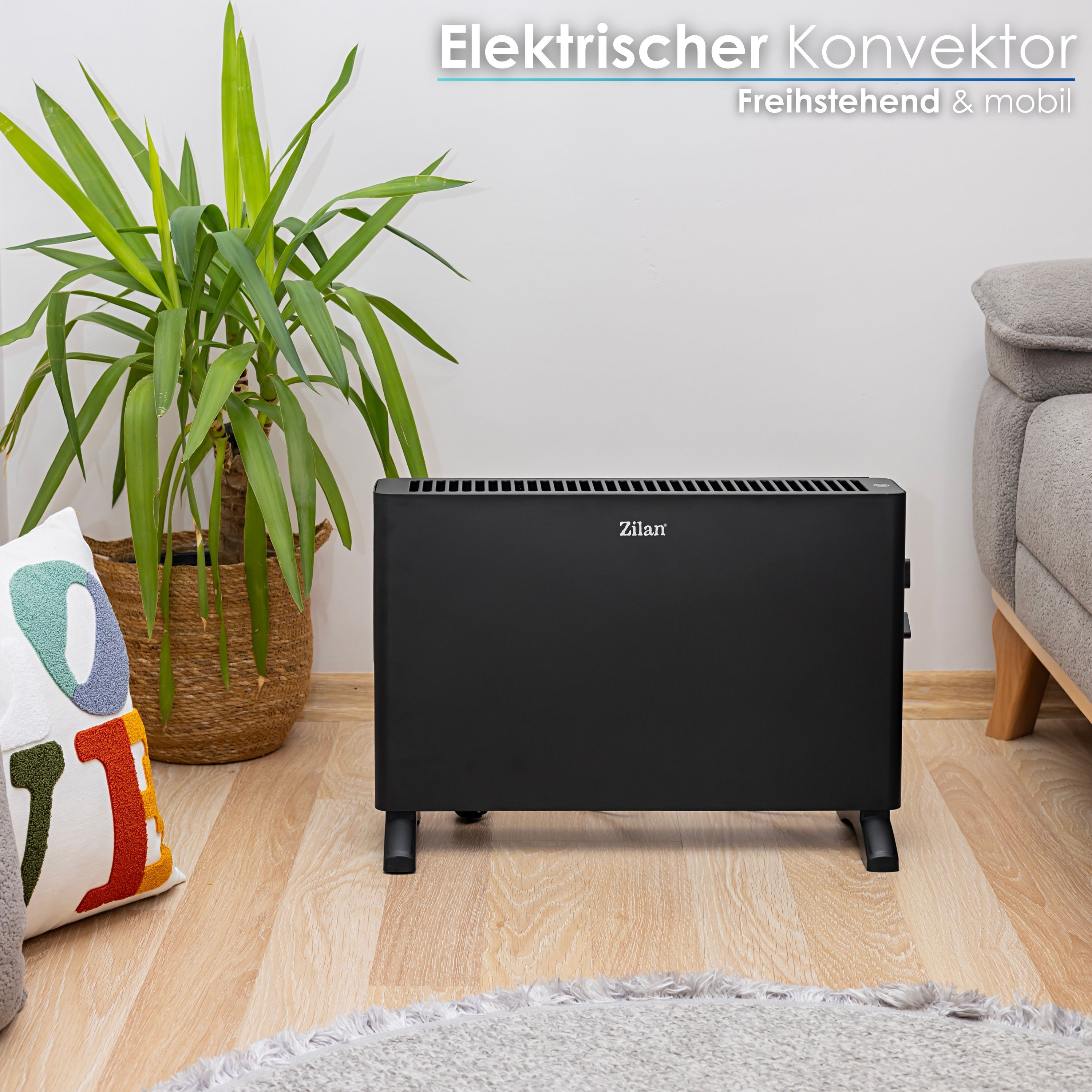 Ein schwarzer Elektroheizer auf Holzboden. Im Hintergrund befinden sich eine Pflanze, ein Kissen und ein Sofa.