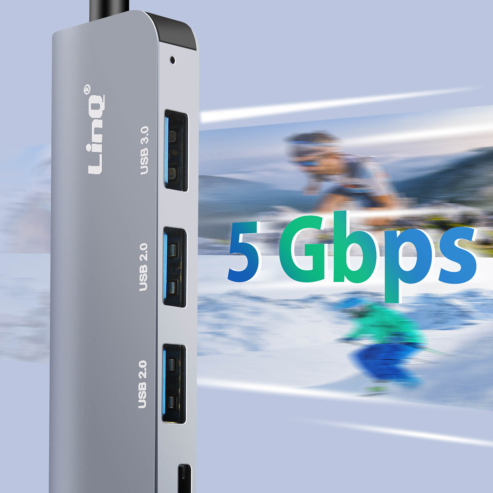 Un hub USB argento con tre porte USB e una porta USB 3.0. Lo sfondo mostra sciatori.