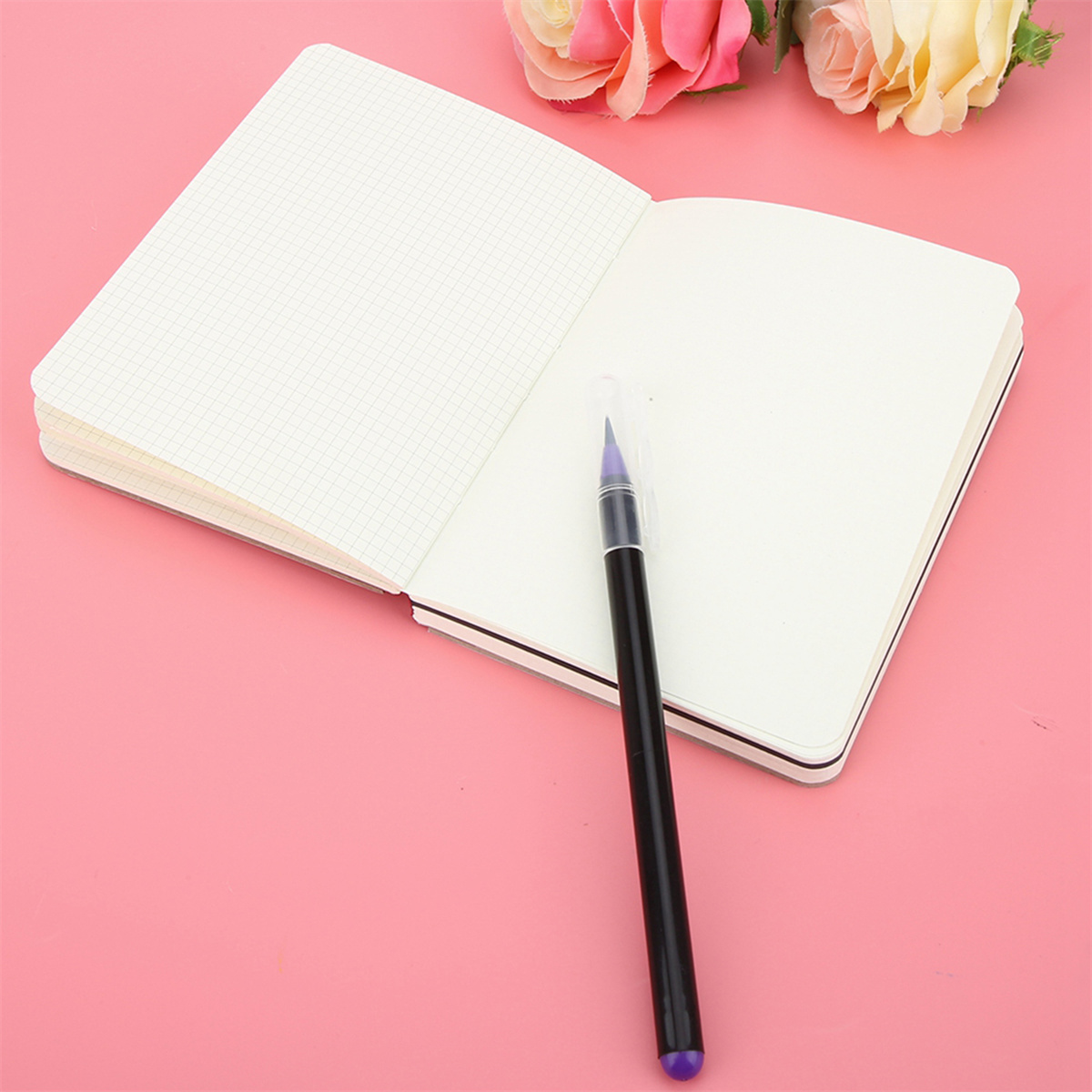 Ein offenes Notizbuch mit Rasterlinien und einem Stift. Rosa Hintergrund, zwei Rosen oben.