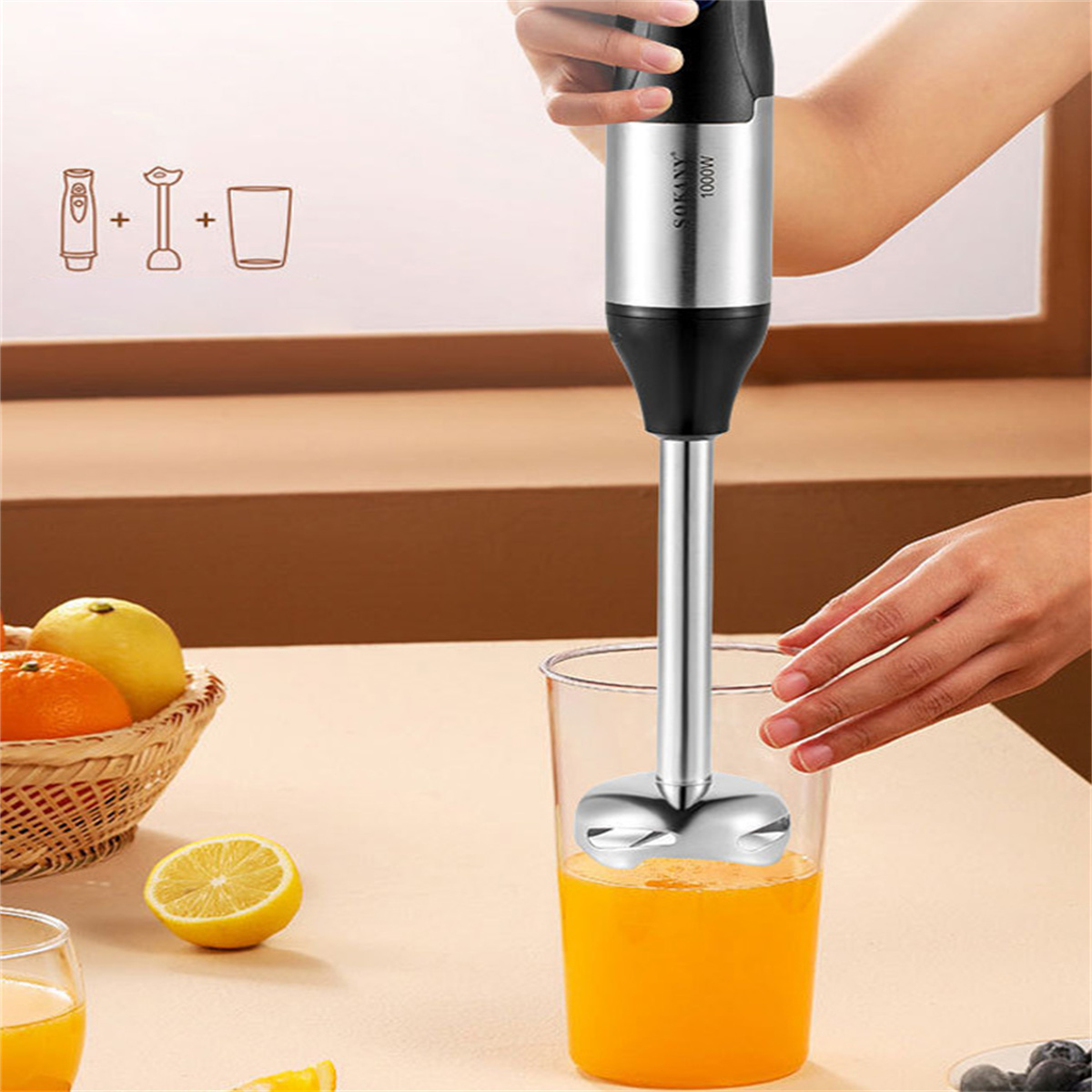 Handmixer, der Orangensaft in einem klaren Glas mixt, mit Früchten und Zubehör.