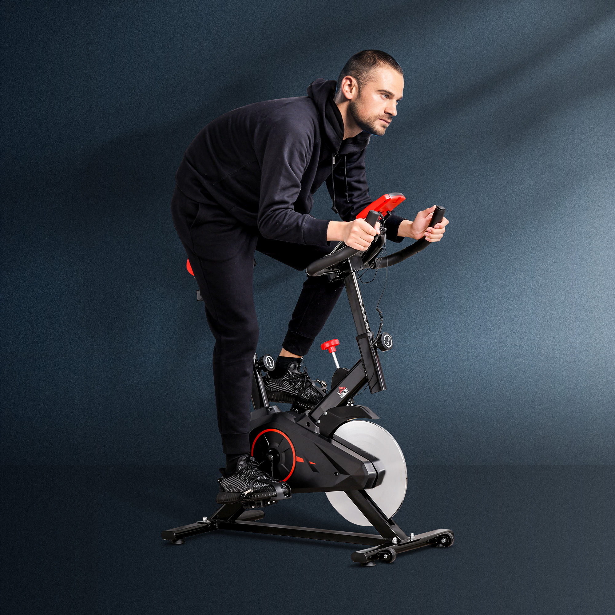 Mann in schwarzer Trainingskleidung auf einem Heimtrainer. Rote Akzente am Fahrrad und dunkler blauer Hintergrund.