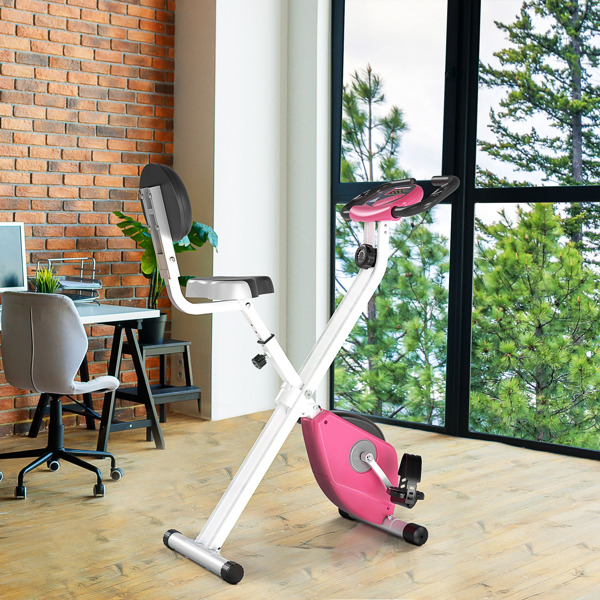 Bicicletta da ciclismo indoor in un ambiente di home office. Muro di mattoni, scrivania e finestra. La bici è rosa e bianca.