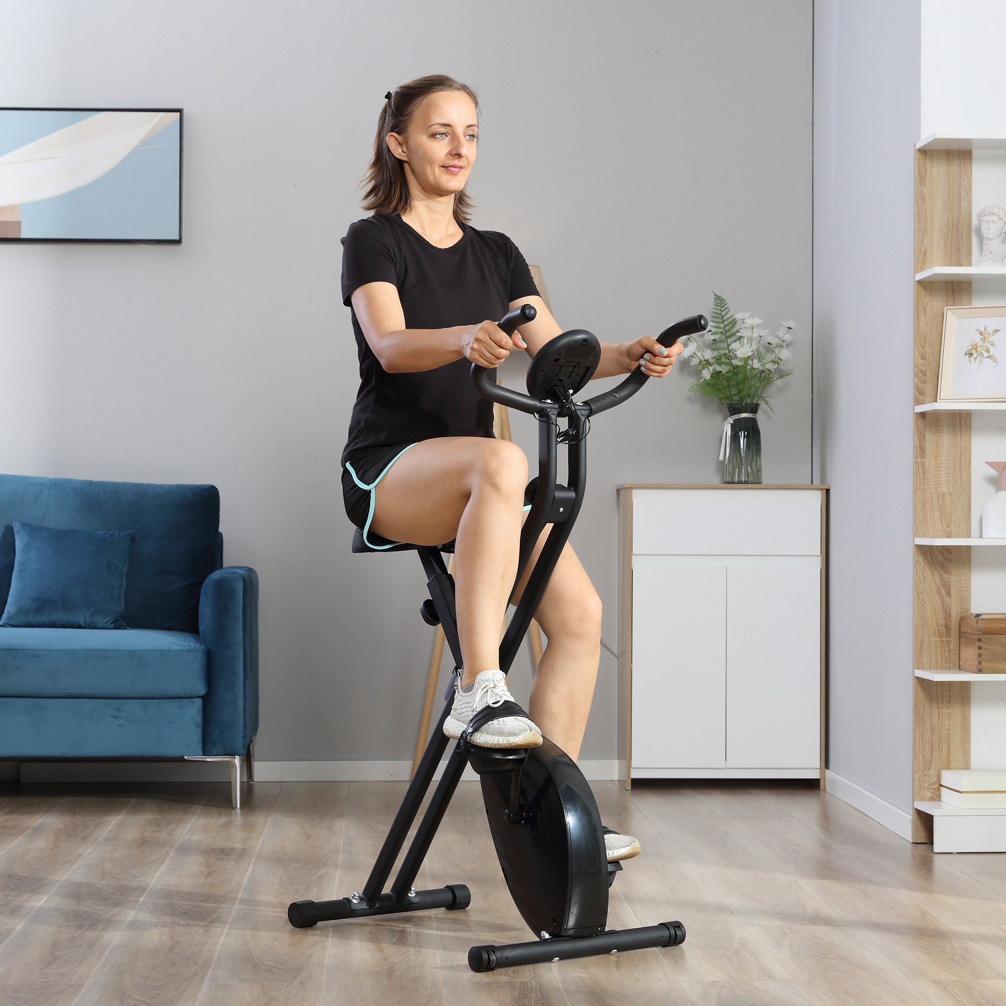 Donna che si esercita su una cyclette pieghevole in una stanza. Divano blu sullo sfondo.