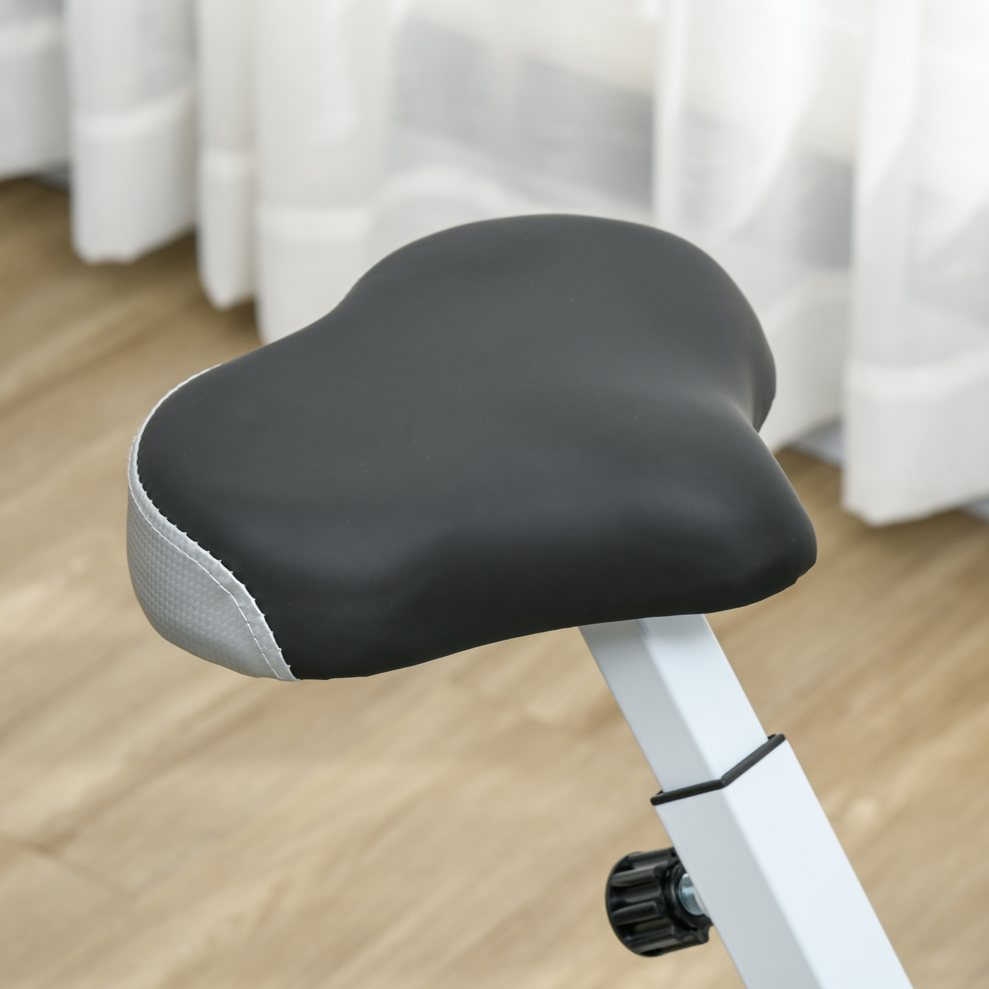 Primo piano di una sella di cyclette nera e grigia. Sfondo bianco.