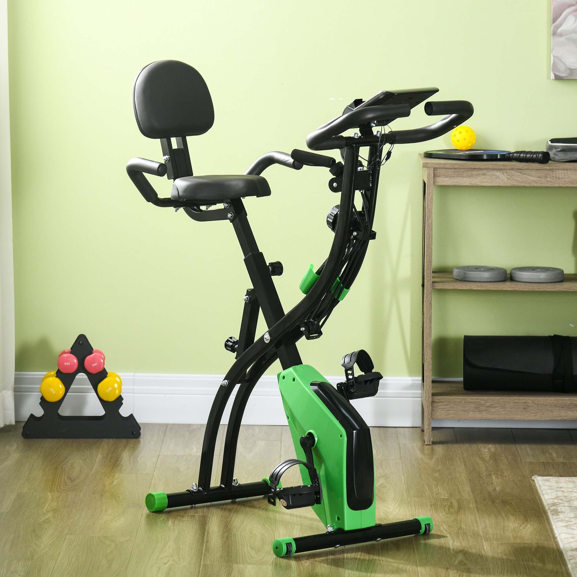 Bicicletta da palestra pieghevole verde e nera in una stanza con parete verde e pavimento in legno.