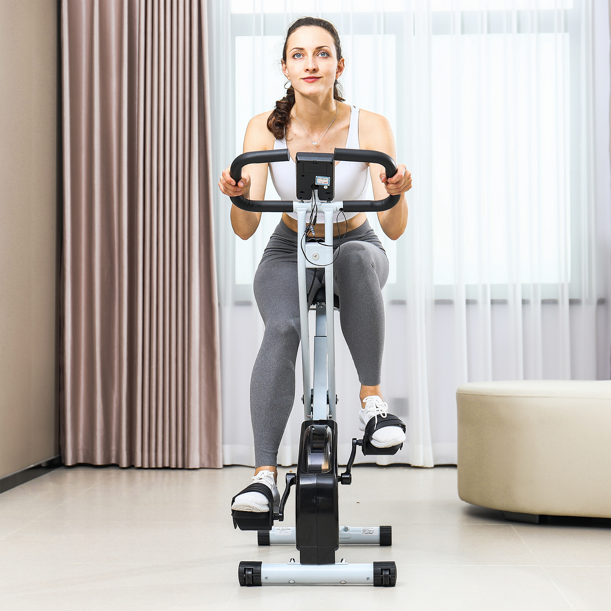 Donna che usa una cyclette pieghevole. Indossa abiti sportivi. Sfondo chiaro.