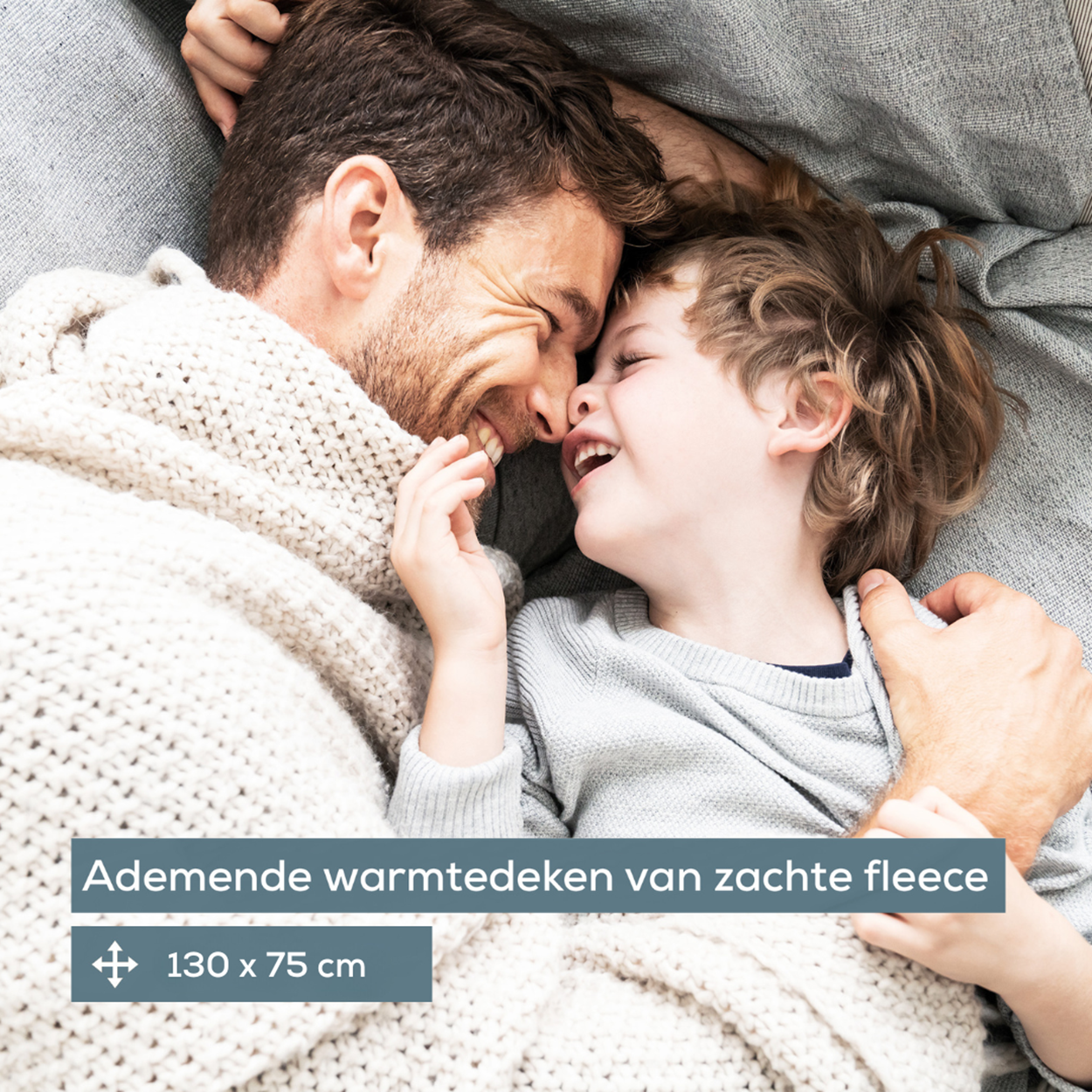Vater und Kind lachen, bedeckt von einer Decke. Text: 'ademende warmtedeken'.