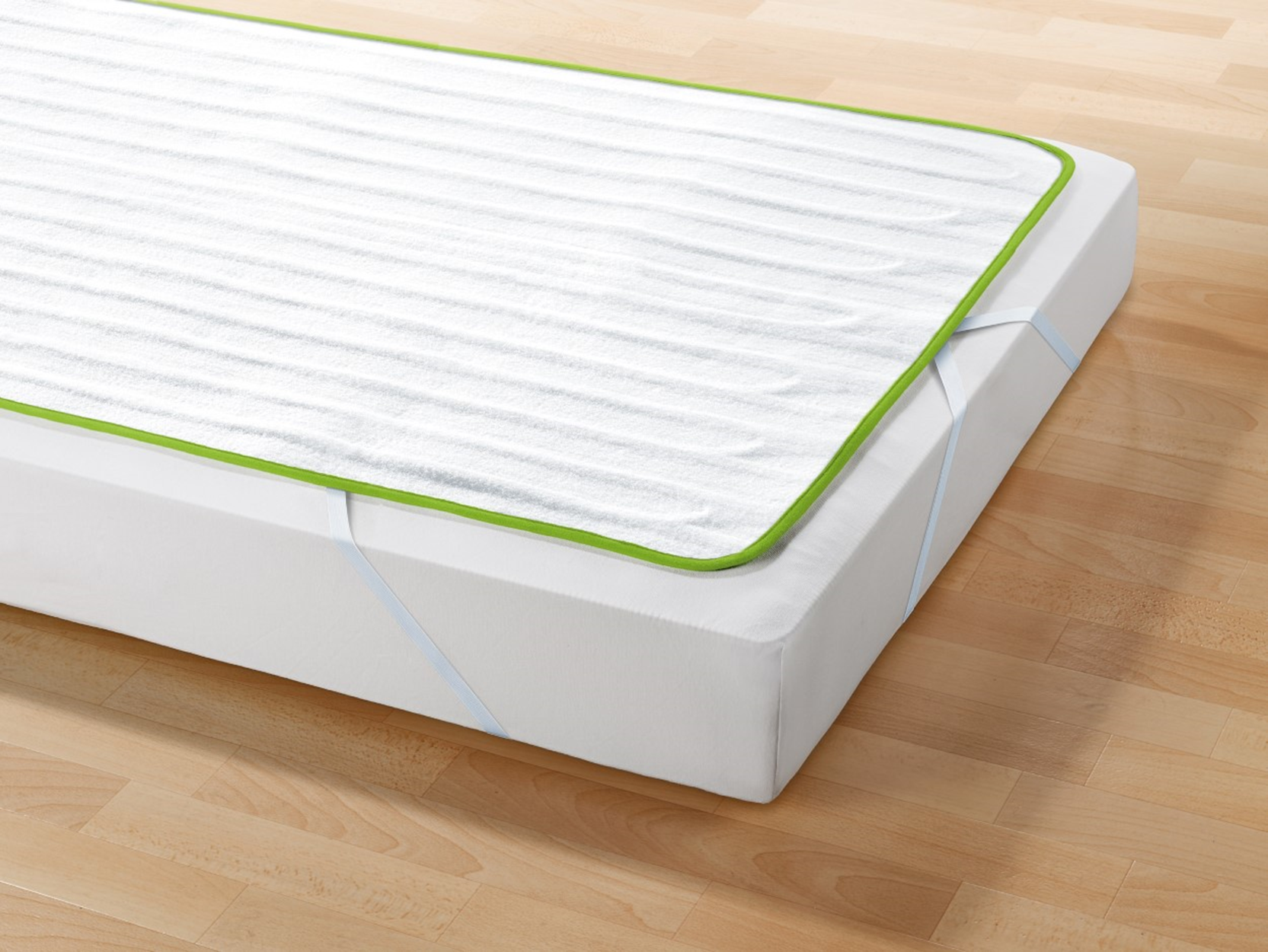 Un protector de colchón blanco con borde verde, sobre un colchón blanco.