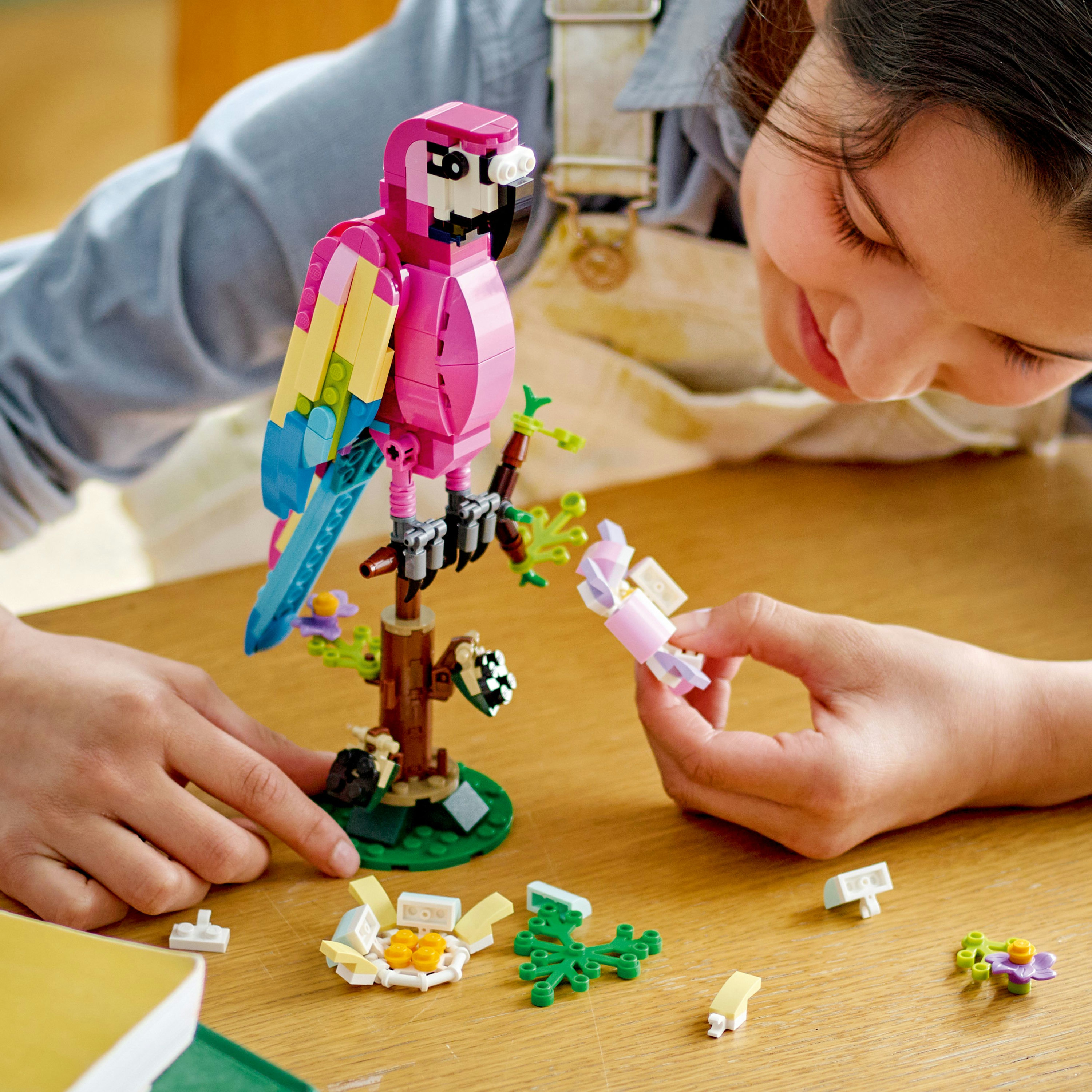 Una ragazza sta costruendo un pappagallo Lego. Il pappagallo è rosa, giallo e blu. La ragazza sorride e guarda il pappagallo.