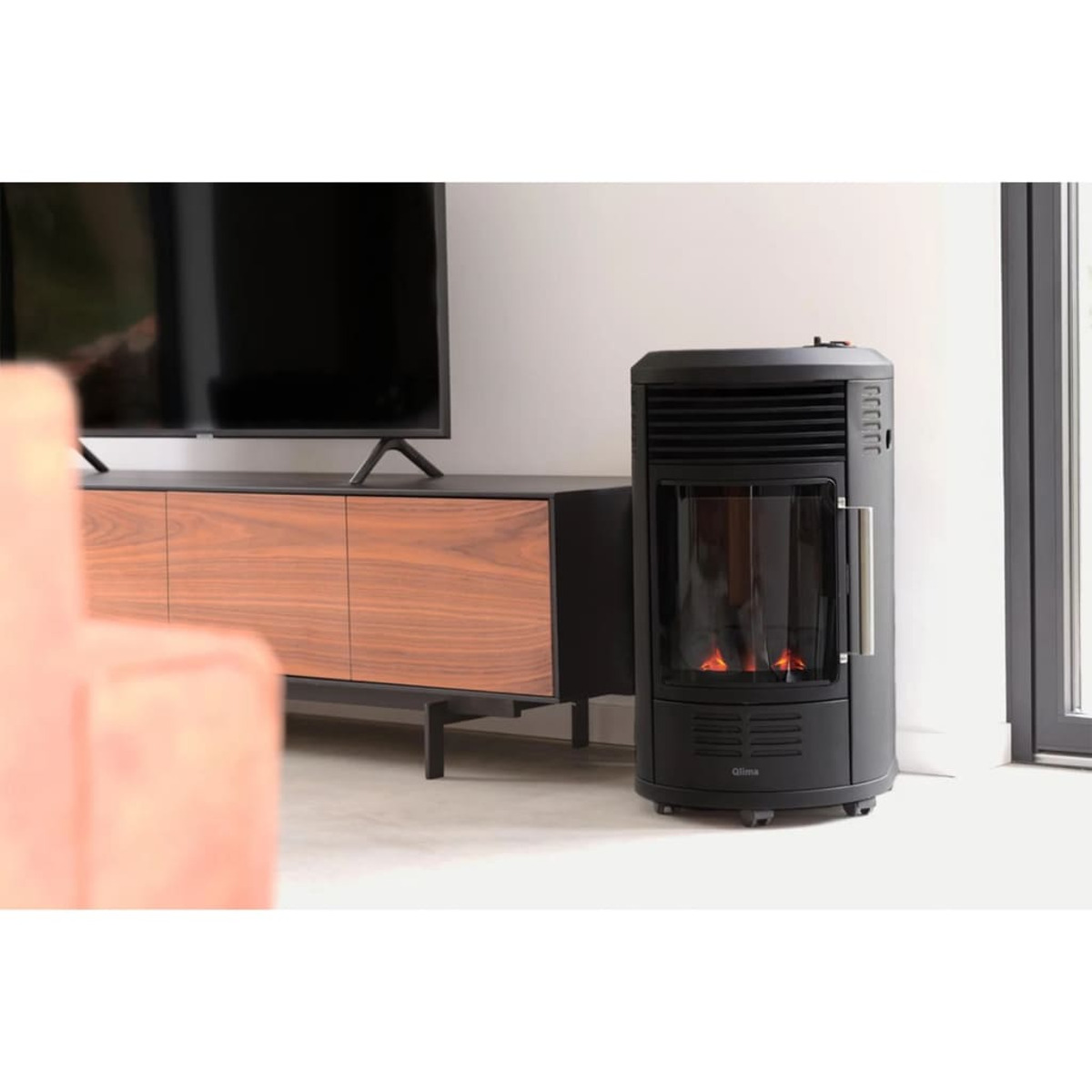 Stufa a pellet nera con fiamme visibili. TV e mobile in legno sullo sfondo.