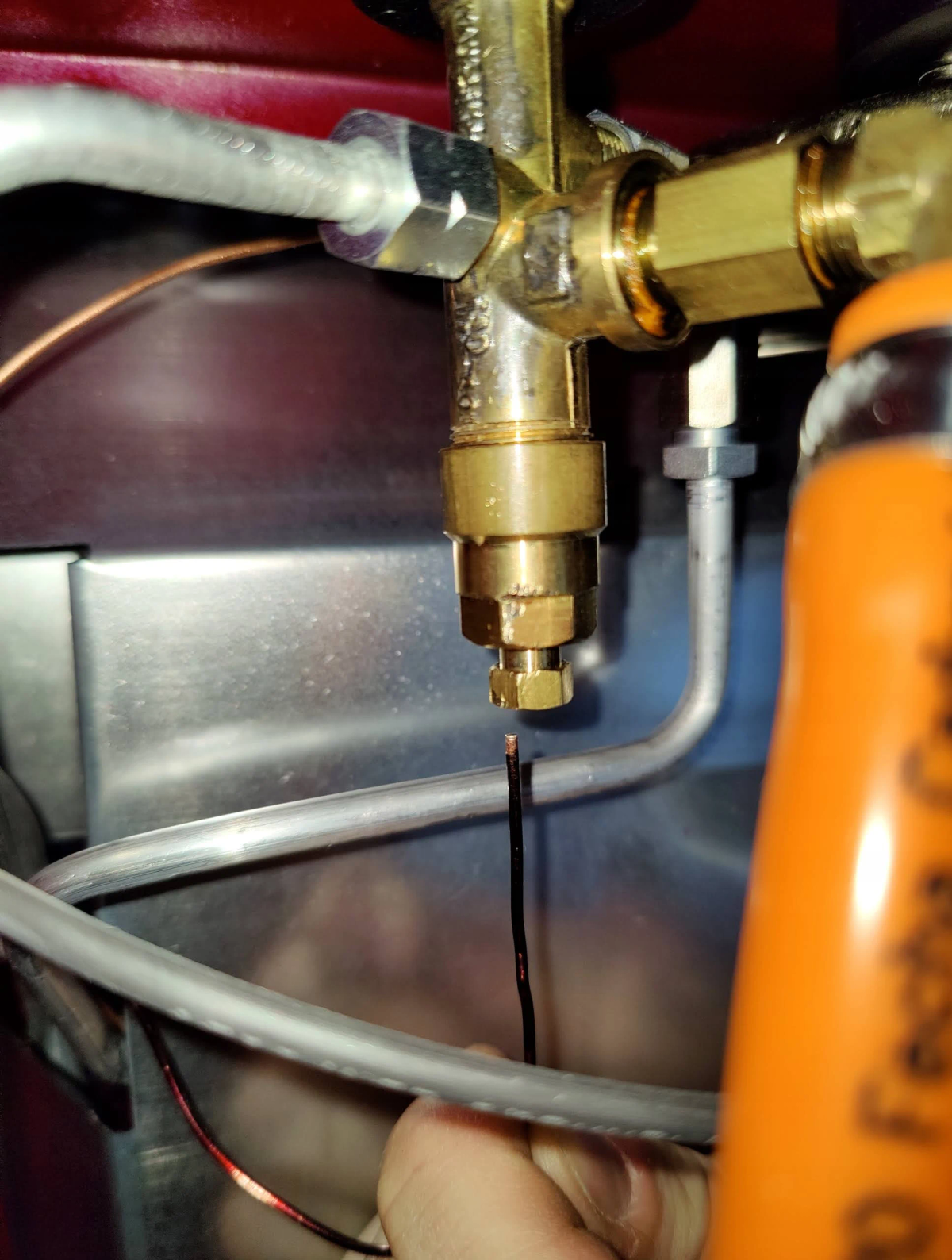 Primer plano de válvula de gas de latón con cables y una lata de gas naranja.