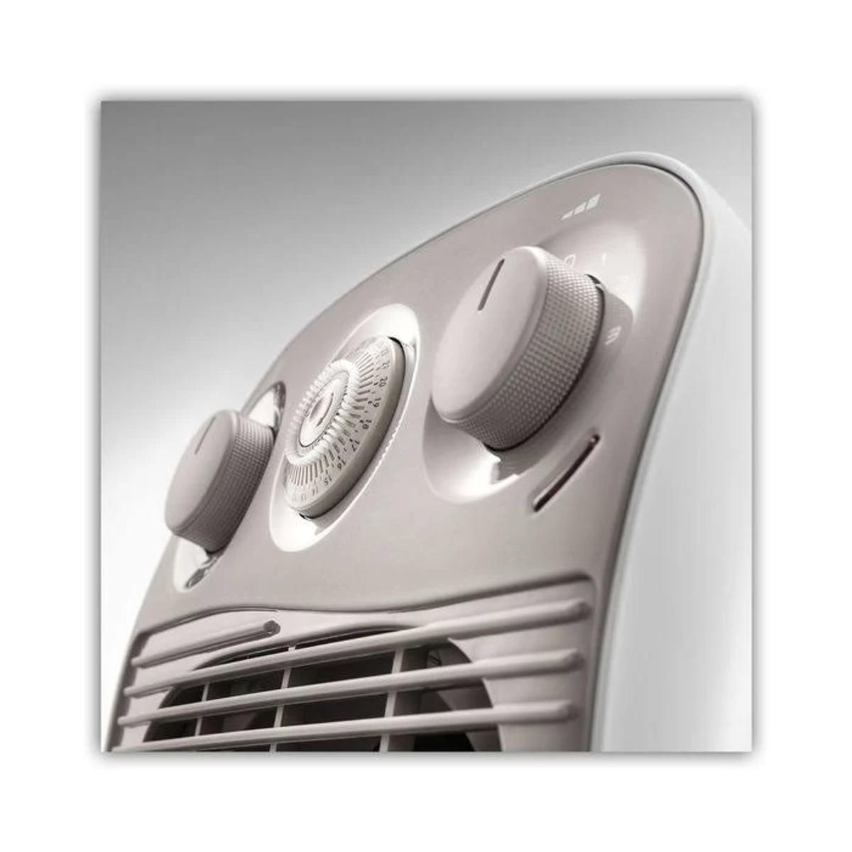 Zbliżenie białego i szarego grzejnika elektrycznego z pokrętłami sterowania i otworem wentylacyjnym, skierowanym w górę.